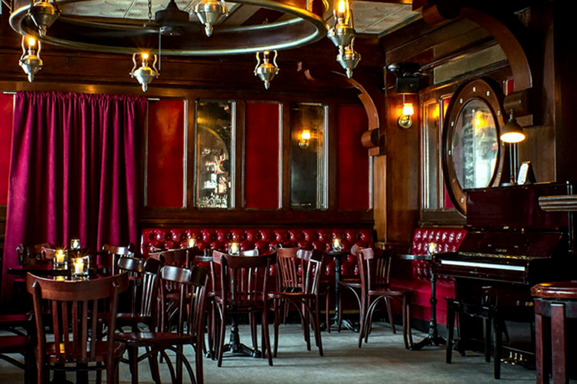 Et interiør af en restaurant eller bar med træpaneler, røde velourgardiner og et klaver. (AI-genereret tekst)