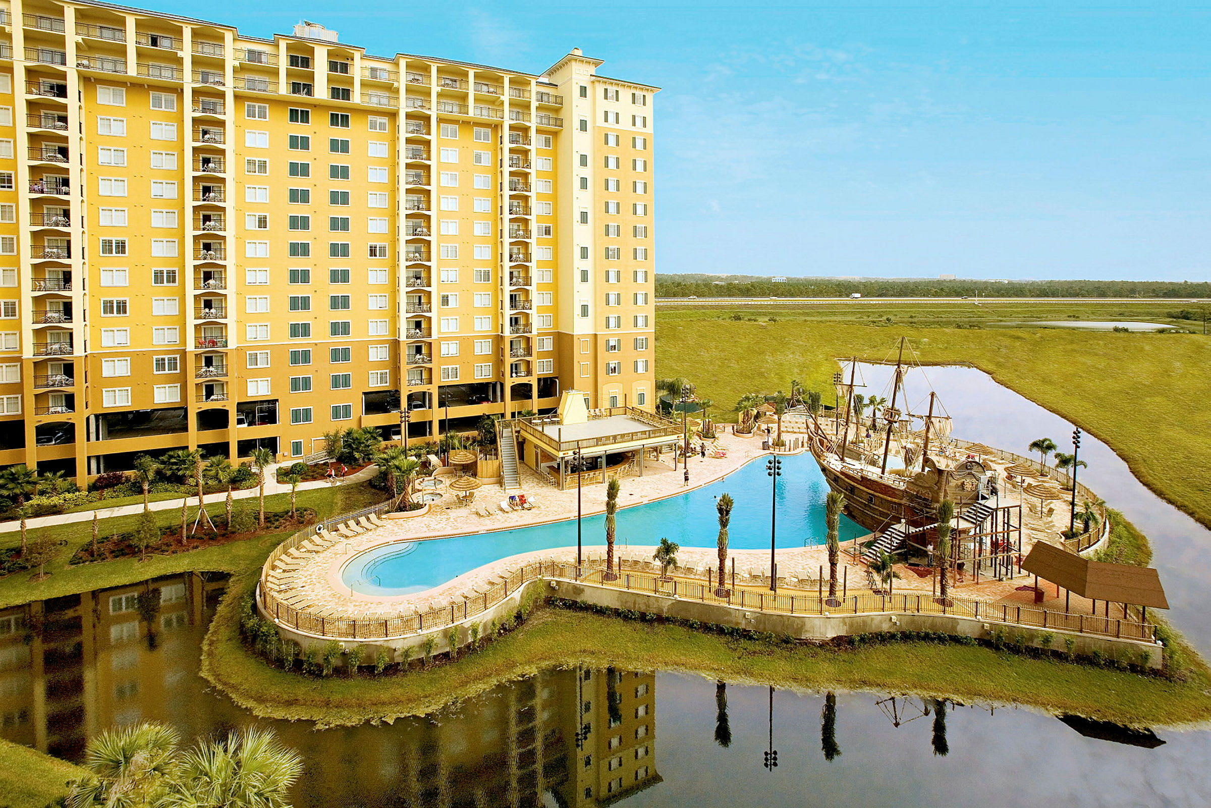 Et større hotel med gul facade, i forgrunden ses en pool og et område med en legeplads der har et pirat temapark. (AI-genereret tekst)