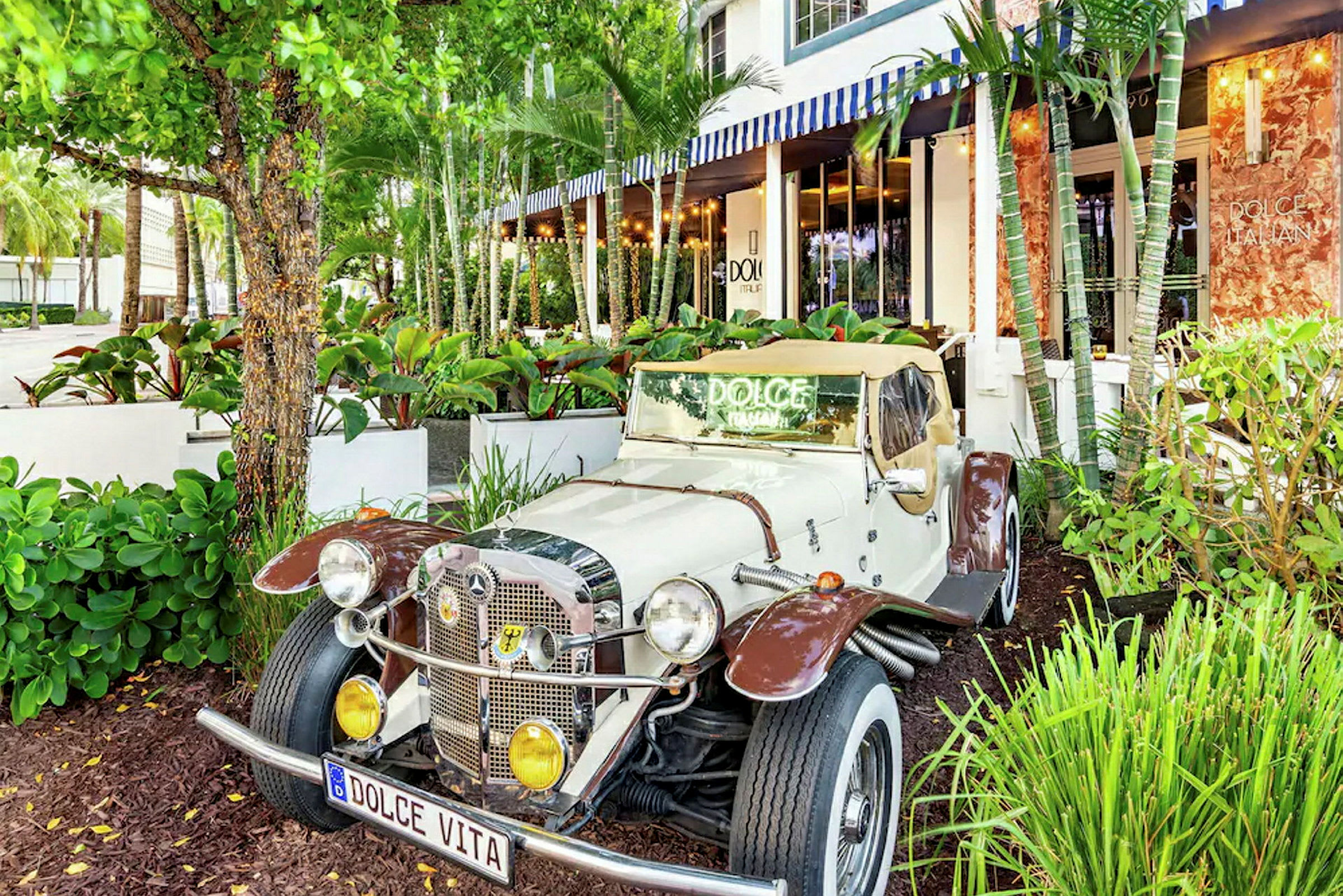 En klassisk bil parkeret foran en restaurant omgivet af frodig vegetation. (AI-genereret tekst)
