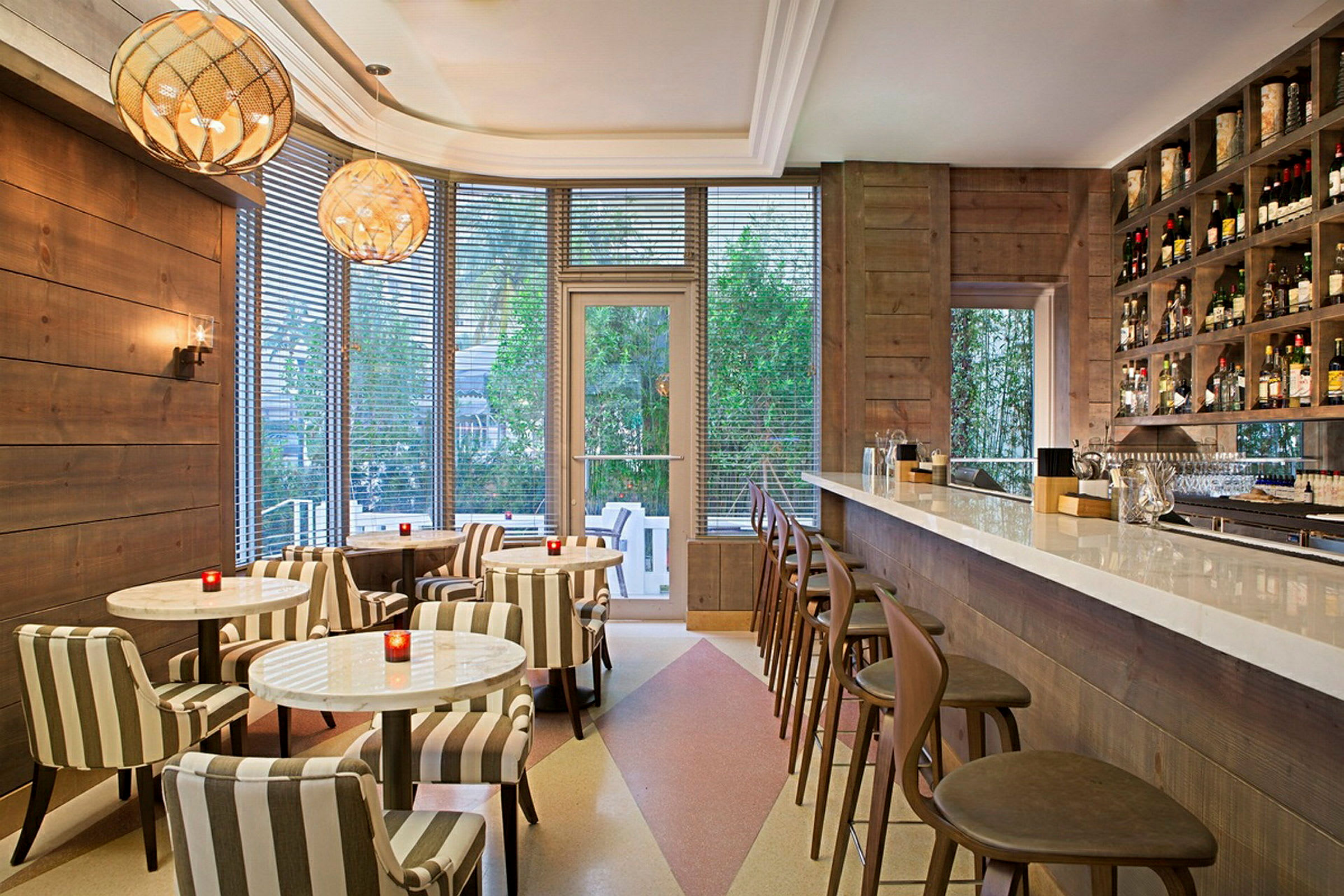 En stilfuldt indrettet café eller bar interiør med lyse møbler, en lang bardisk til højre og borde med stole til venstre. (AI-genereret tekst)