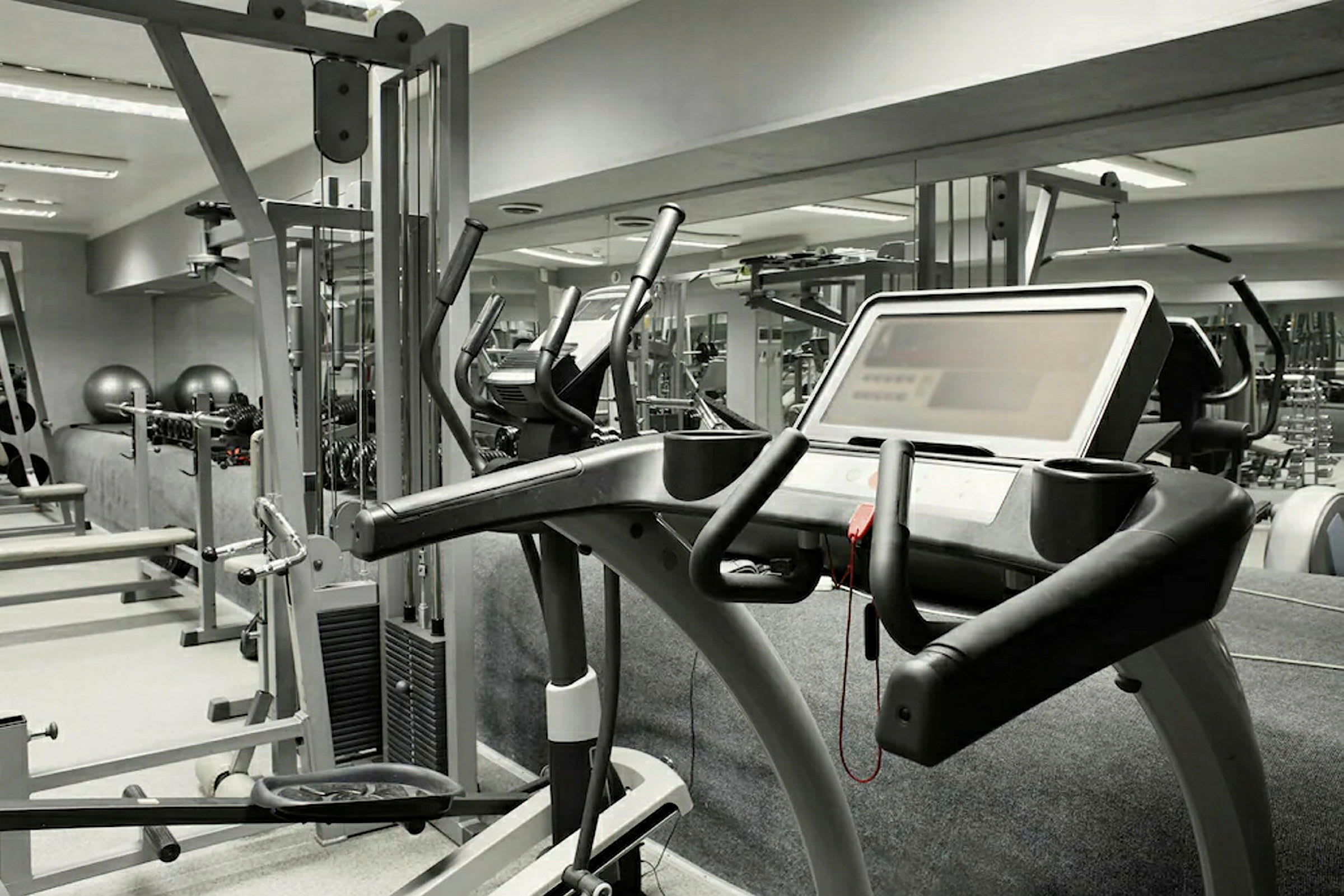 Et fitnesscenter med forskellige træningsmaskiner, herunder et løbebånd i forgrunden. (AI-genereret tekst)
