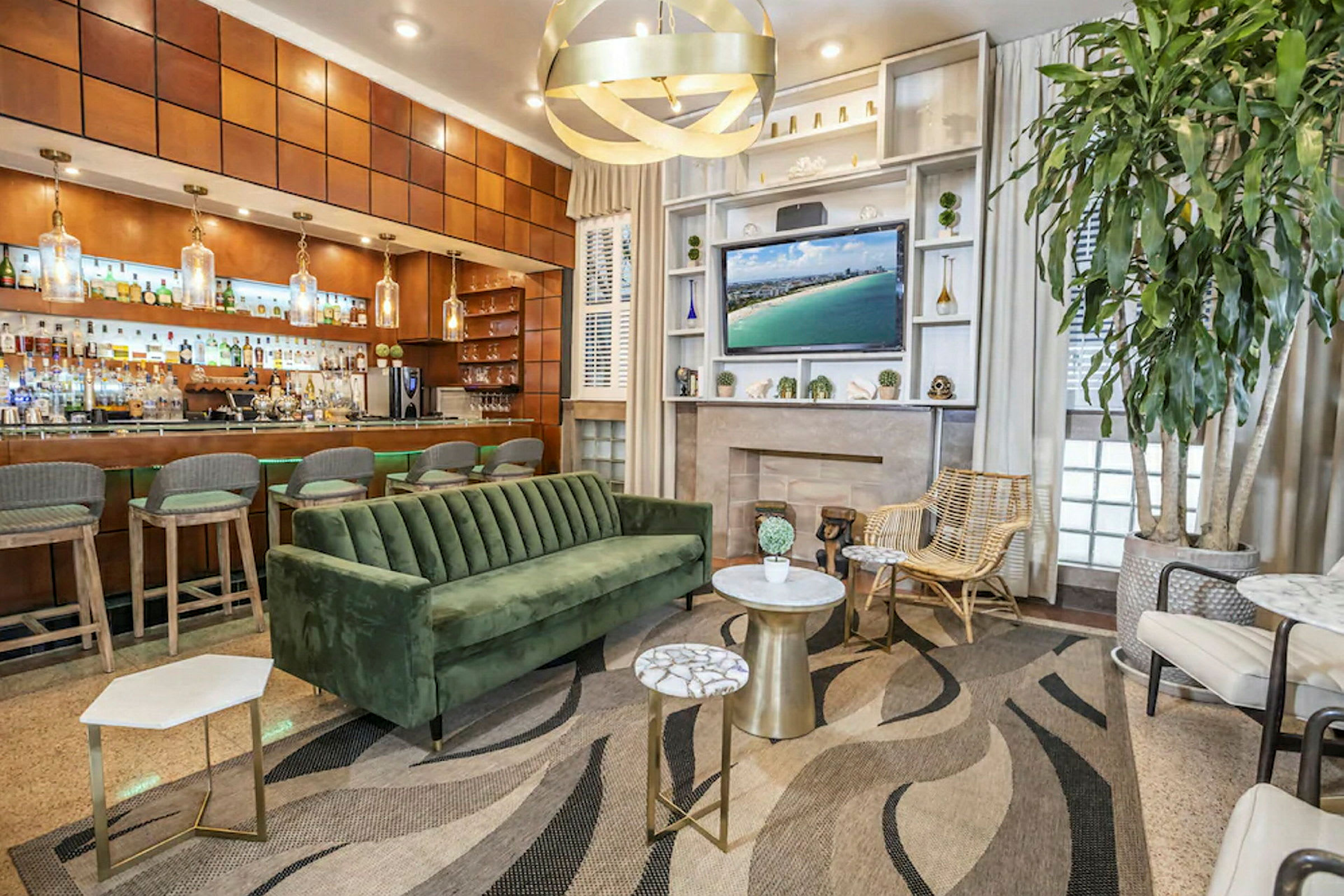 Et moderne loungeområde med en grøn fløjlssofa, flere små borde, en stor plante og en bar i baggrunden. (AI-genereret tekst)