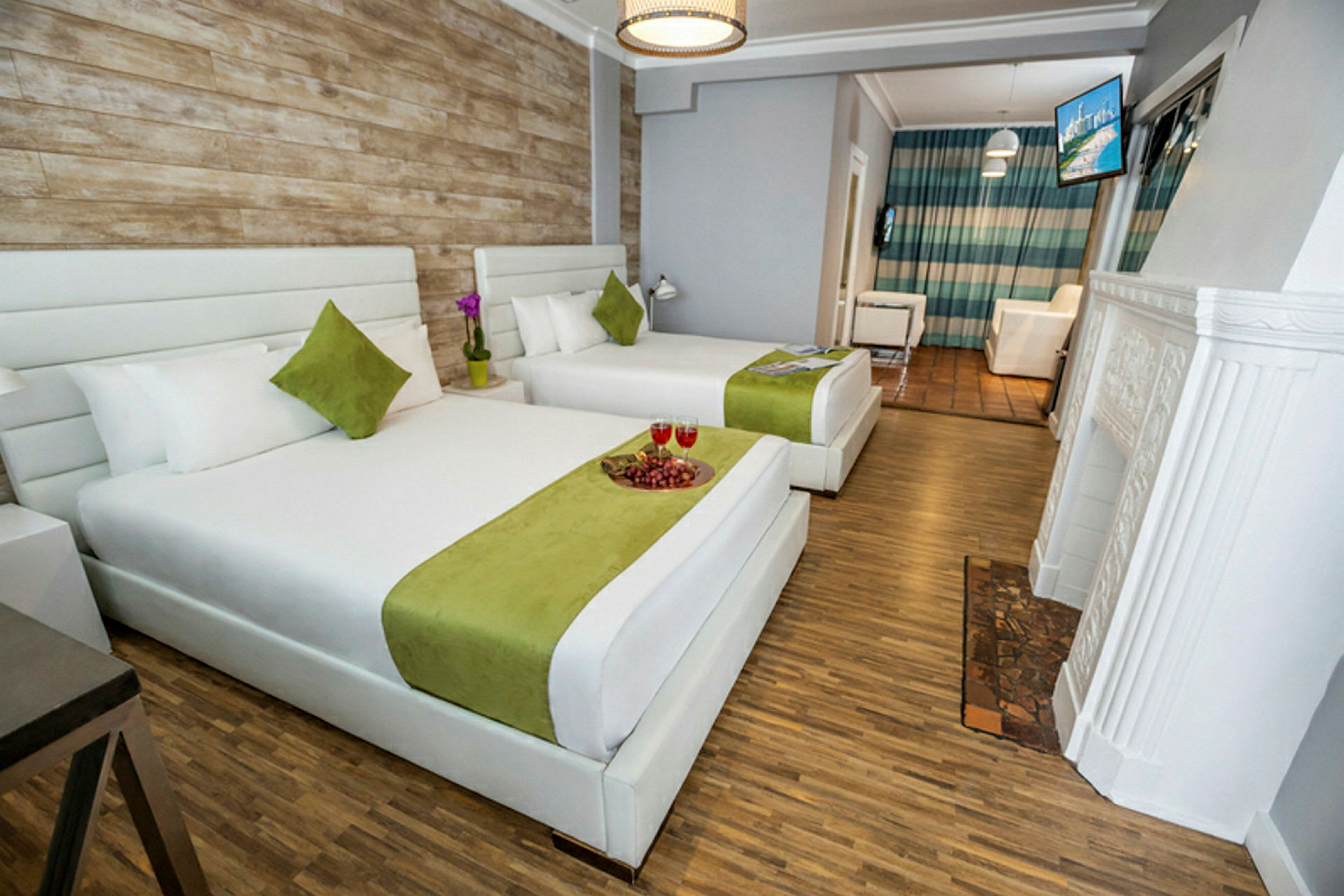 Hotelværelse med to store senge med hvidt og grønt sengelinned, et trægulv og en væg i rustik stil. (AI-genereret tekst)