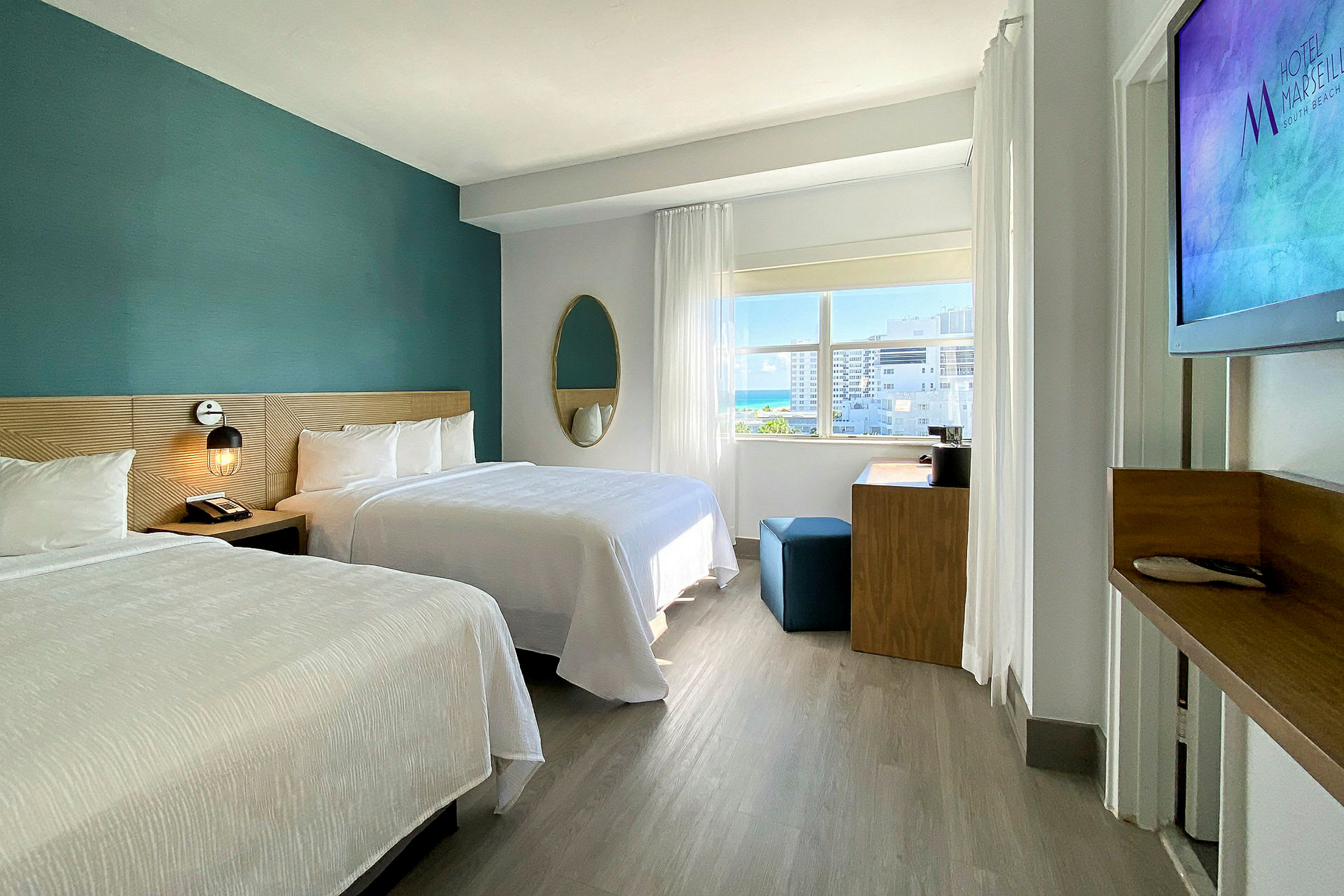 Et moderne hotelværelse med to dobbeltsenge, et skrivebord og et stort vindue, der lader naturligt lys komme ind. (AI-genereret tekst)