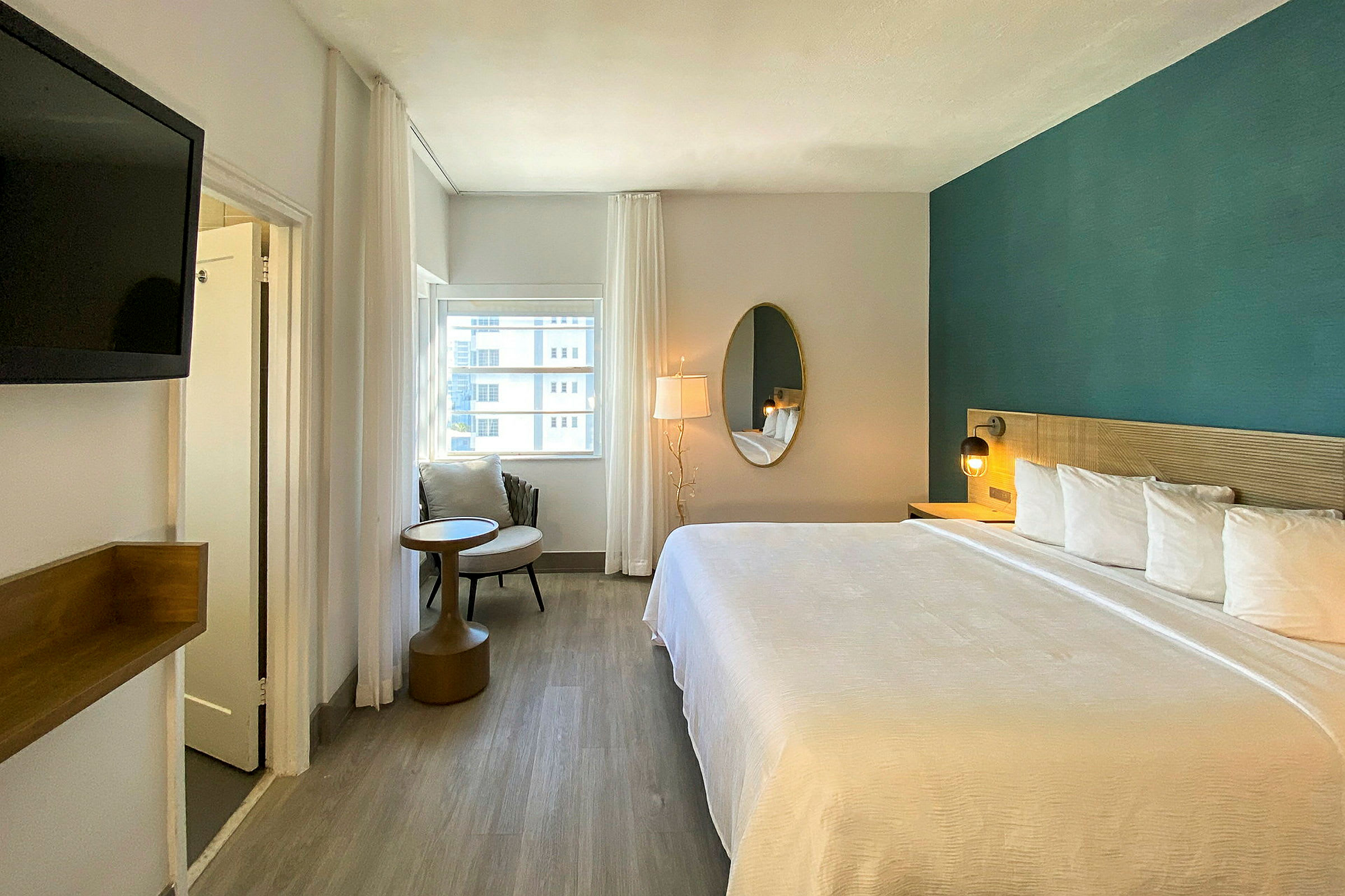 Moderne indrettet hotelværelse med stor seng, spejl, lænestol og udsigt fra vinduet. (AI-genereret tekst)