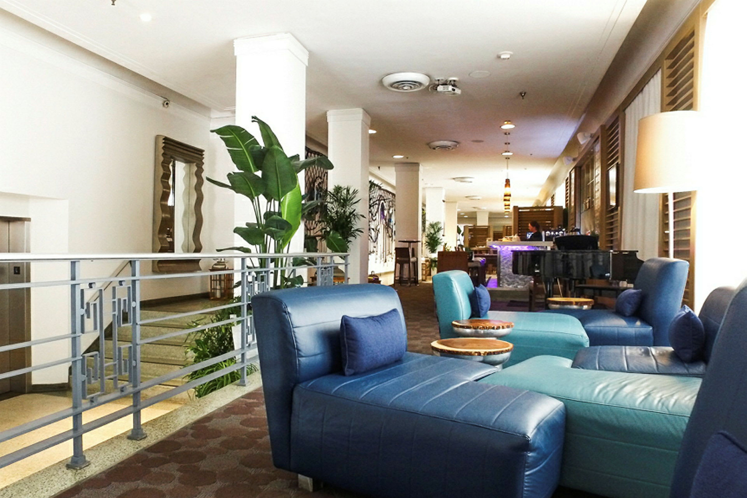 Billede af en hotellobby med blå siddepladser, grønne planter og en bar i baggrunden. (AI-genereret tekst)