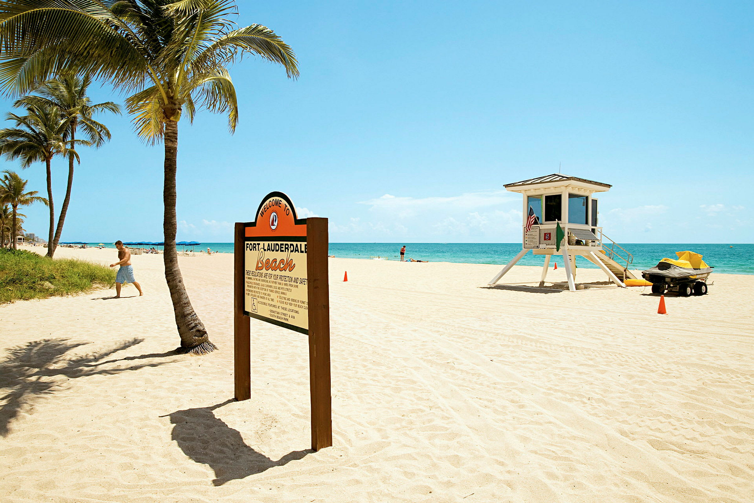 En sandstrand med palmer, et skilt der byder velkommen til Fort Lauderdale Beach og et livreddertårn. (AI-genereret tekst)