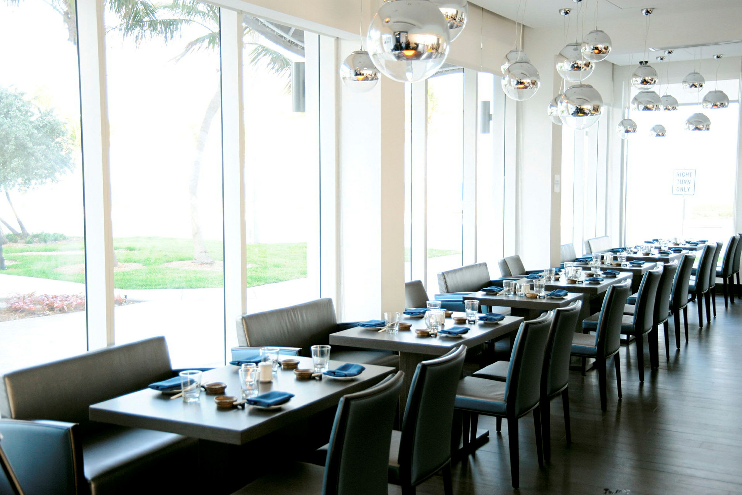 En moderne restaurant med flere dækkede borde, udsigt over grønne områder og store vinduer. (AI-genereret tekst)