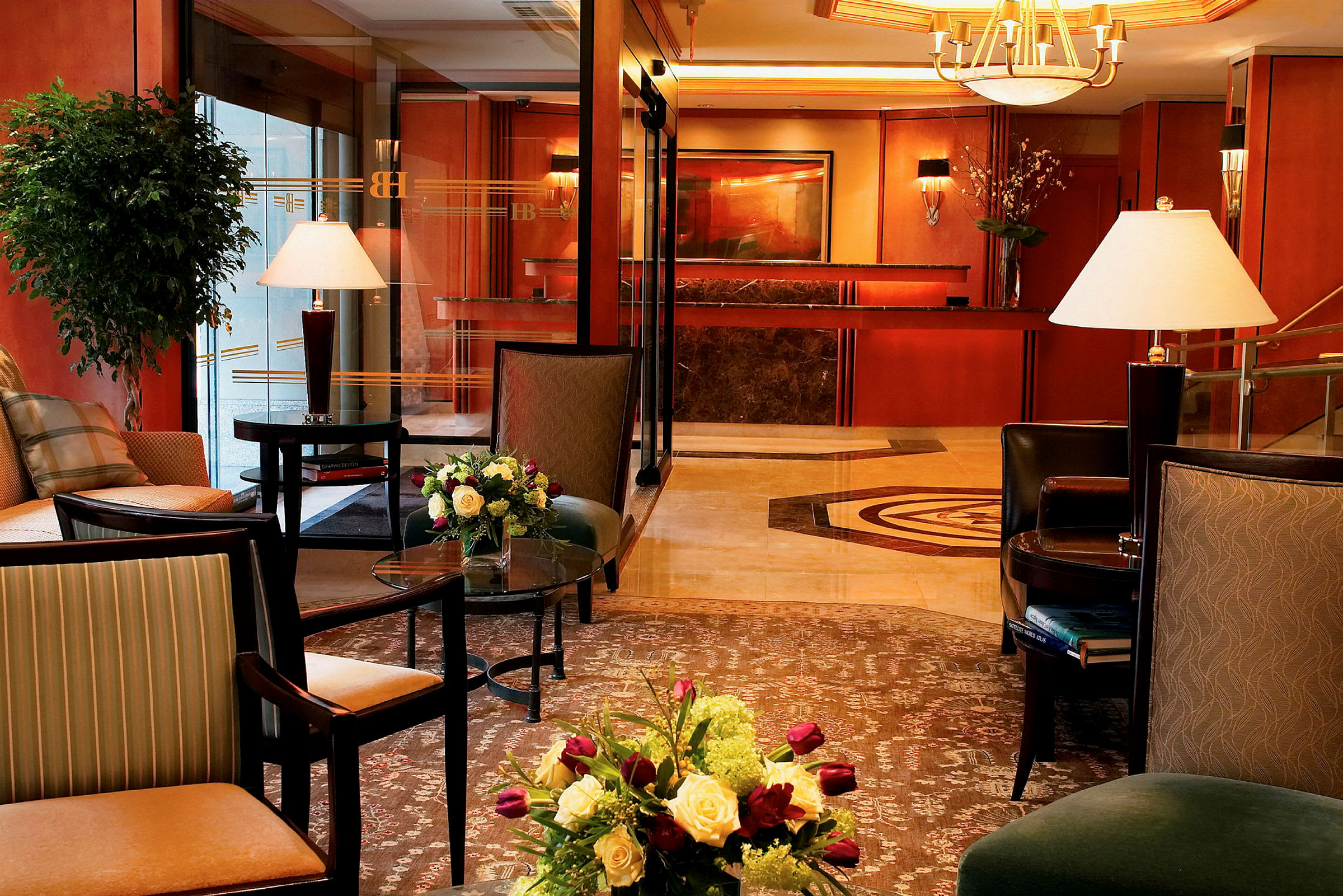 Et smagfuldt indrettet hotellobbyområde med møblerede siddeområder, interiørdetaljer, blomsterarrangementer og receptionen i baggrunden. (AI-genereret tekst)
