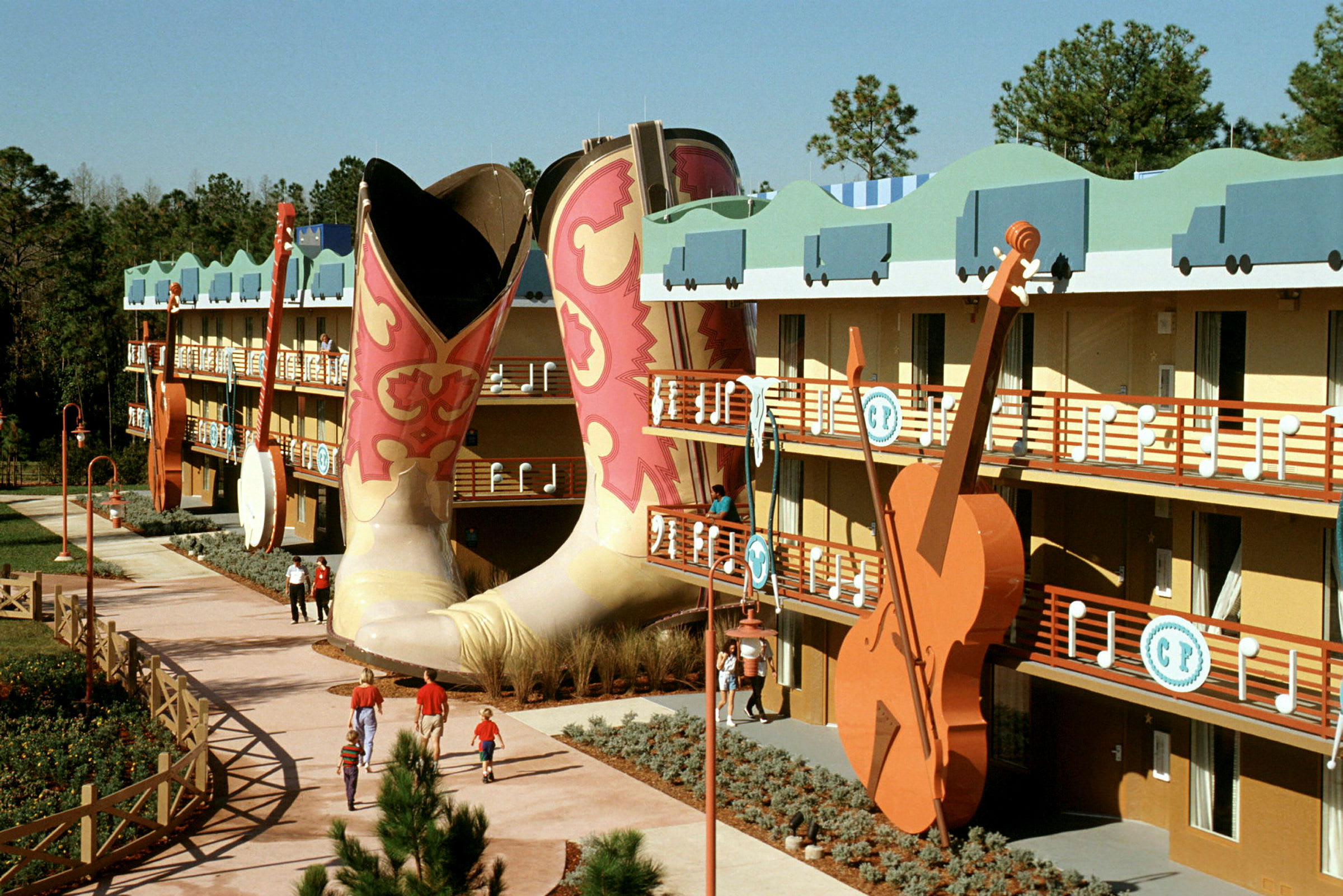 Et farverigt hotelkompleks med store cowboyboots og en guitar i udsmykningen. Folk spadserer på gangstien. (AI-genereret tekst)