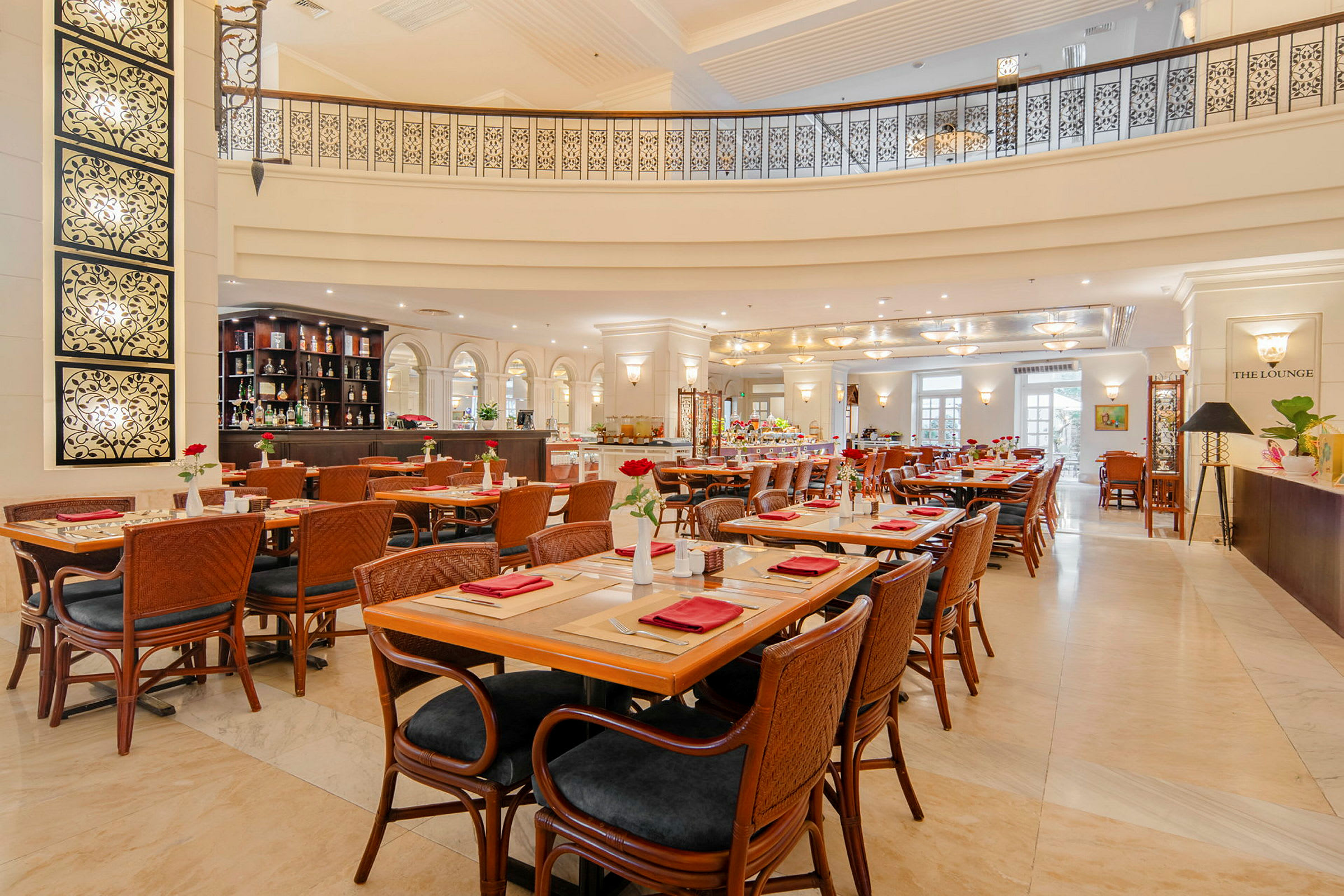 Elegant restaurant med borde og stole i træ, dekoreret med røde servietter og blomster. Bar og lys indretning ses i baggrunden. (AI-genereret tekst)