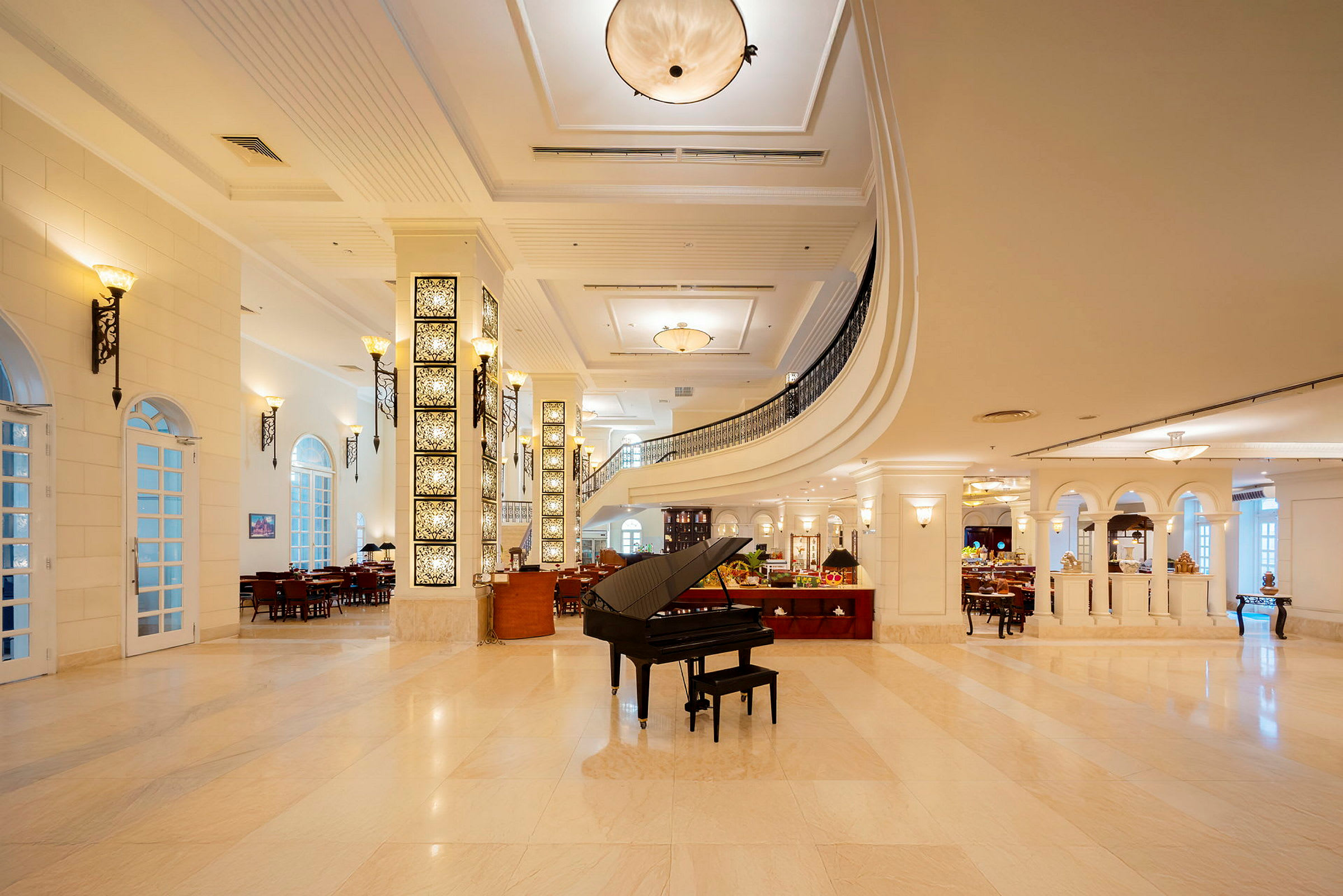 Et elegant hotelatrium med store vinduer, buer og lyse marmorgulve. Et sort flygel står på gulvet i midten. (AI-genereret tekst)