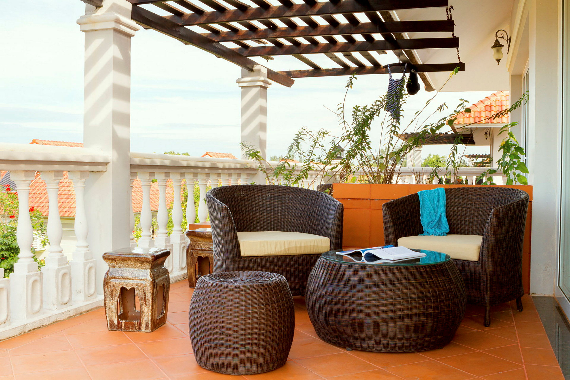 En terrasse med havemøbler i flet, to stole og et bord på et flisebelagt område under en træpergola. (AI-genereret tekst)