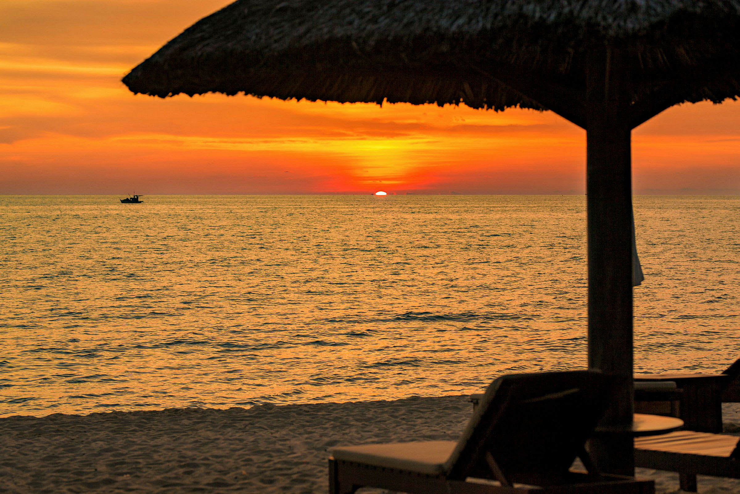 Solnedgang over havet med en strand i forgrunden og silhuetter af liggestole og parasoller. (AI-genereret tekst)