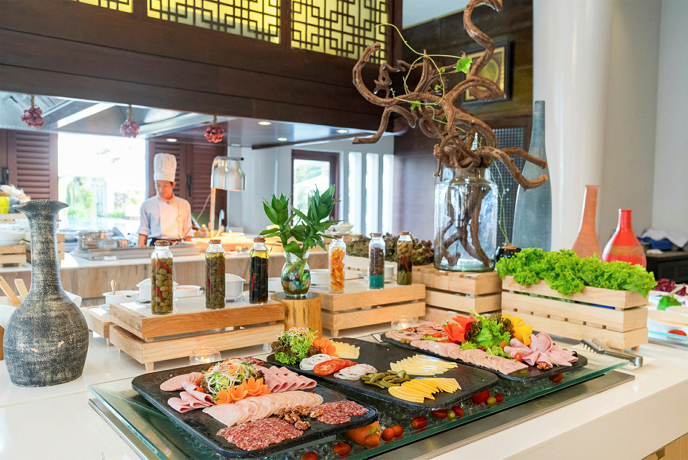 Billede af en buffet med pålæg, oste og salat, omgivet af dekorative detaljer og serveringsudstyr. En kok ses i baggrunden. (AI-genereret tekst)