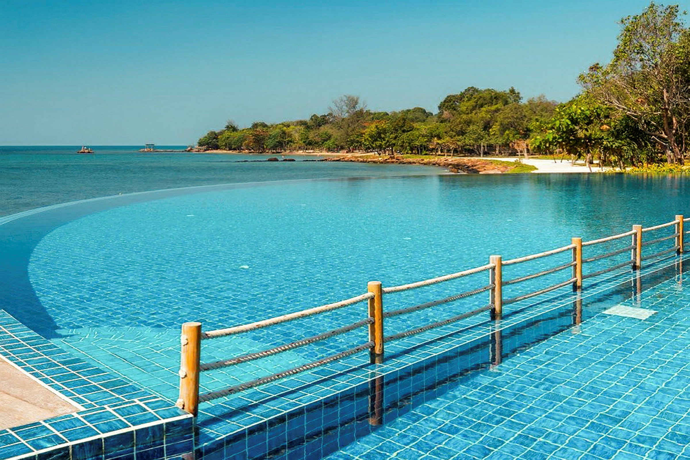 En infinity-pool ved en kyst med klart blåt vand og omkringliggende grøntområder. (AI-genereret tekst)