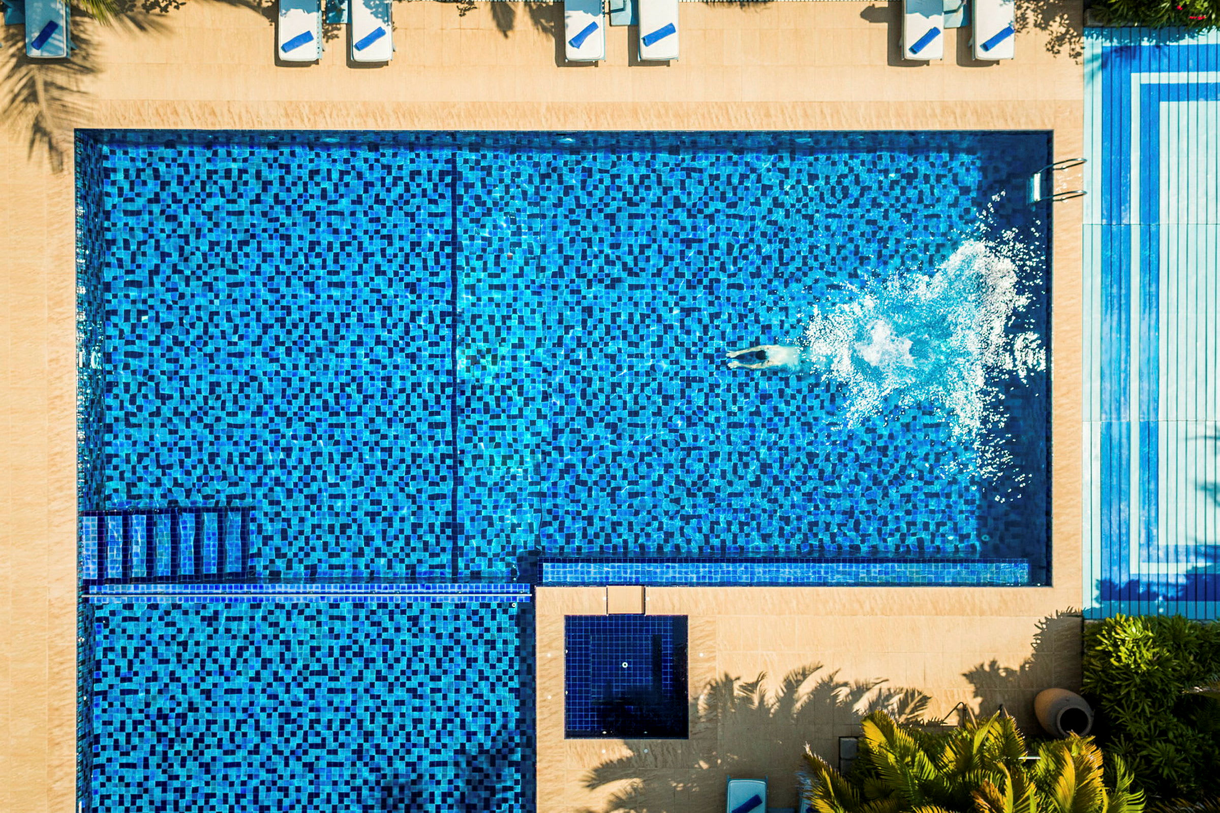 Luftfoto af en swimmingpool med blå mosaik og en person, der svømmer i vandet. (AI-genereret tekst)
