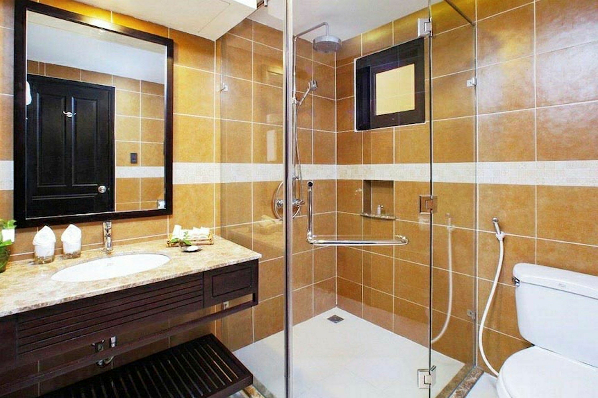 Et badeværelse med brune vægfliser, moderne håndvask og spejl, toilet og bruser med glasvæg. (AI-genereret tekst)