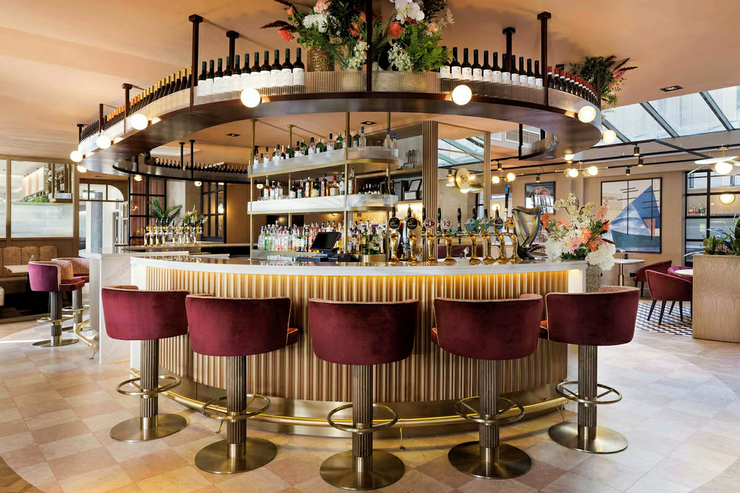 En elegant bar med vinflasker på hylder, blomsterarrangement og siddepladser med røde fløjlsstole. (AI-genereret tekst)