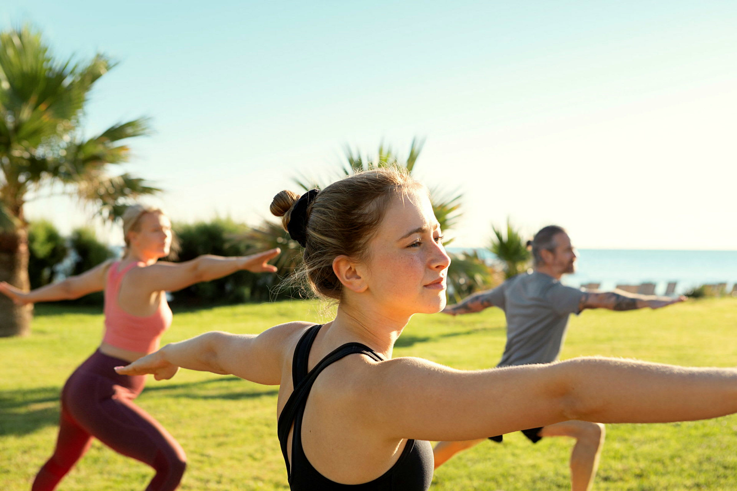 Personer, der dyrker yoga i en grøn park med havet i baggrunden. (AI-genereret tekst)