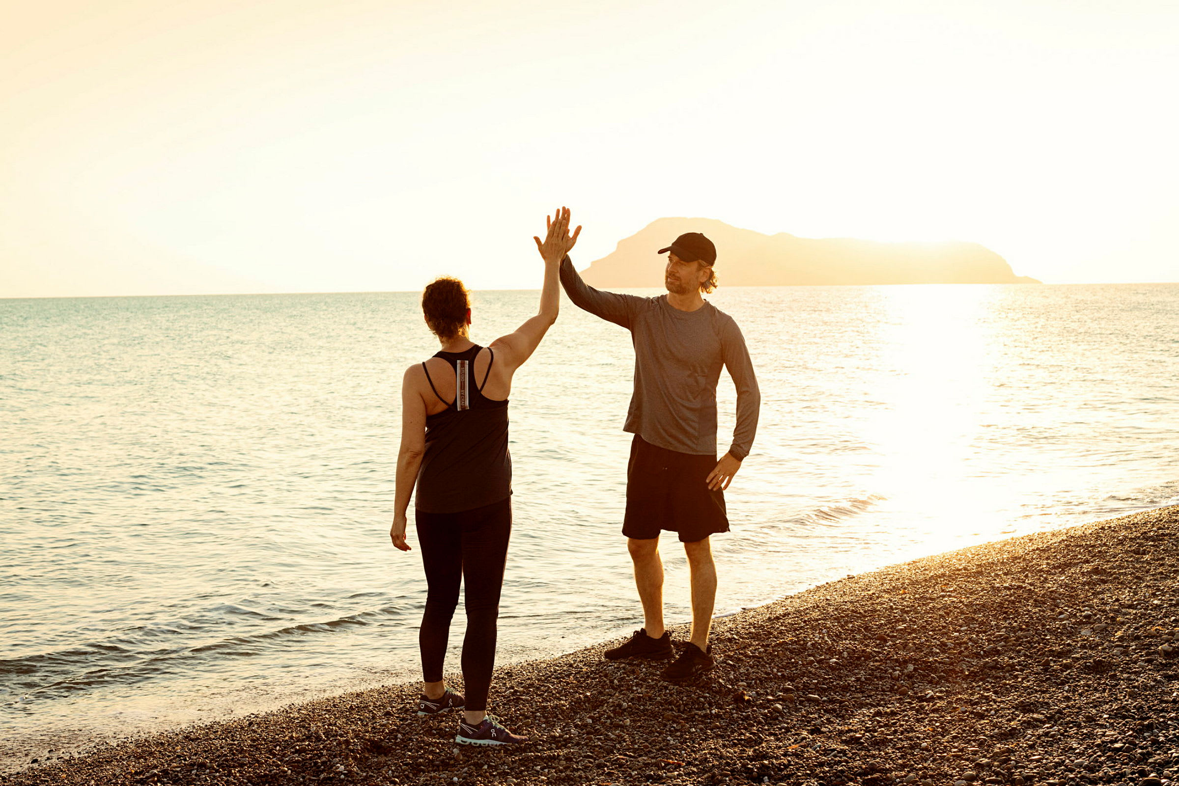 To personer står på en stenstrand og giver hinanden en high five under solnedgangen over havet. (AI-genereret tekst)