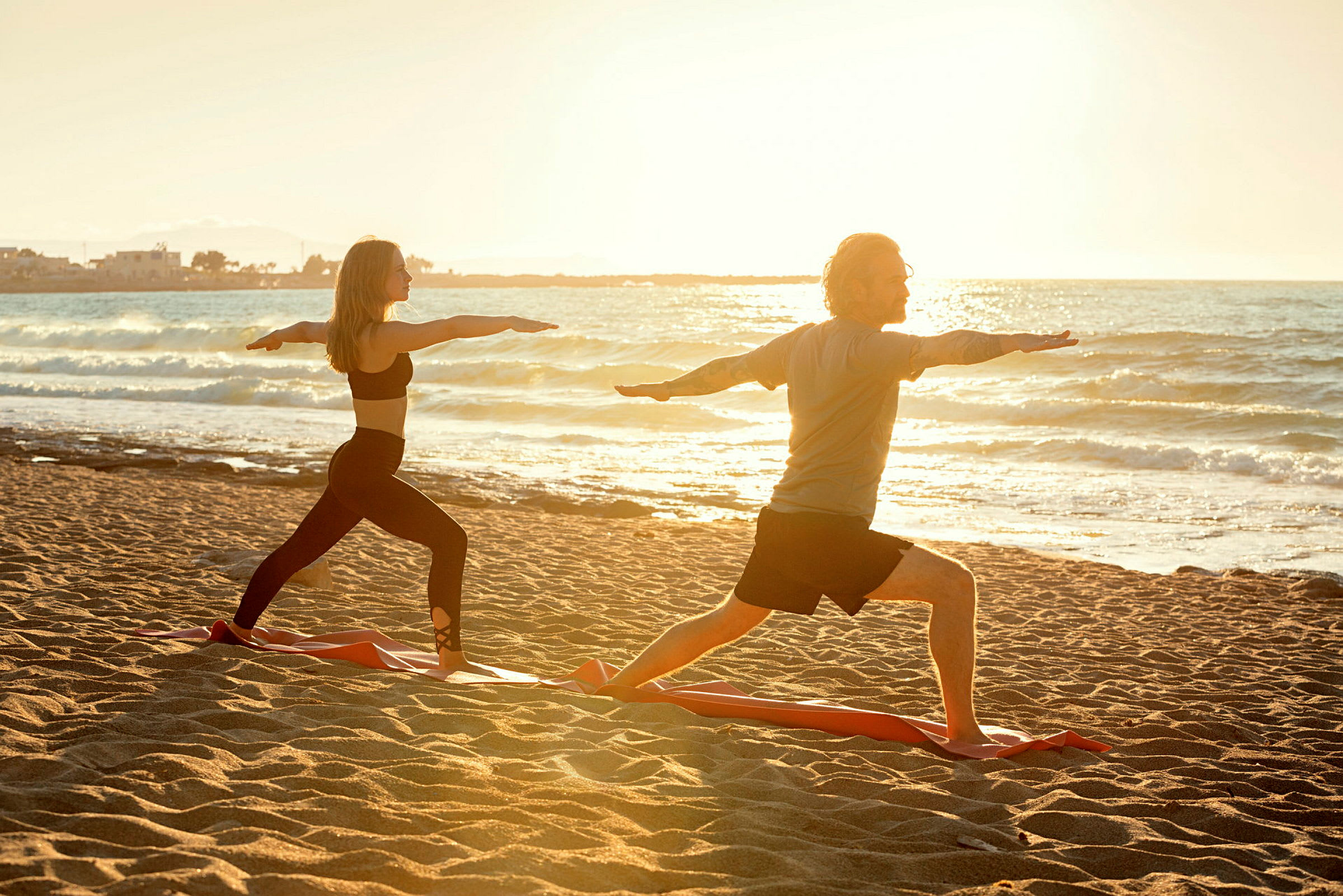 To personer udfører yogaøvelser på en sandstrand ved havet, med solen der går ned i det fjerne. (AI-genereret tekst)