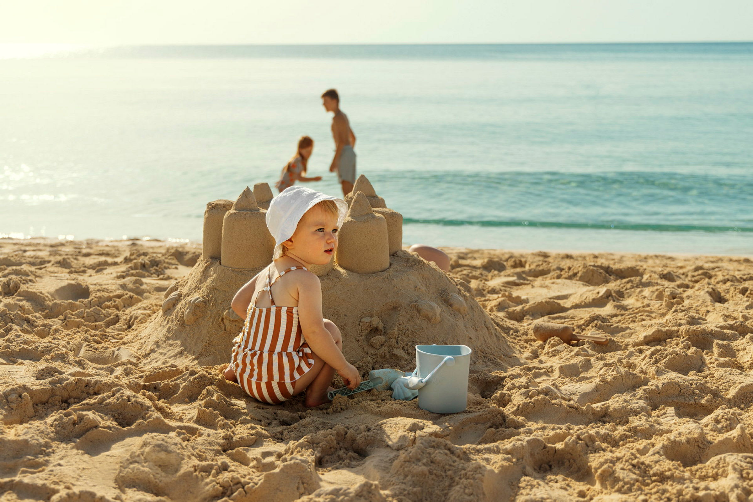 Barn, der bygger et sandslot på stranden med en spand ved siden af. (AI-genereret tekst)