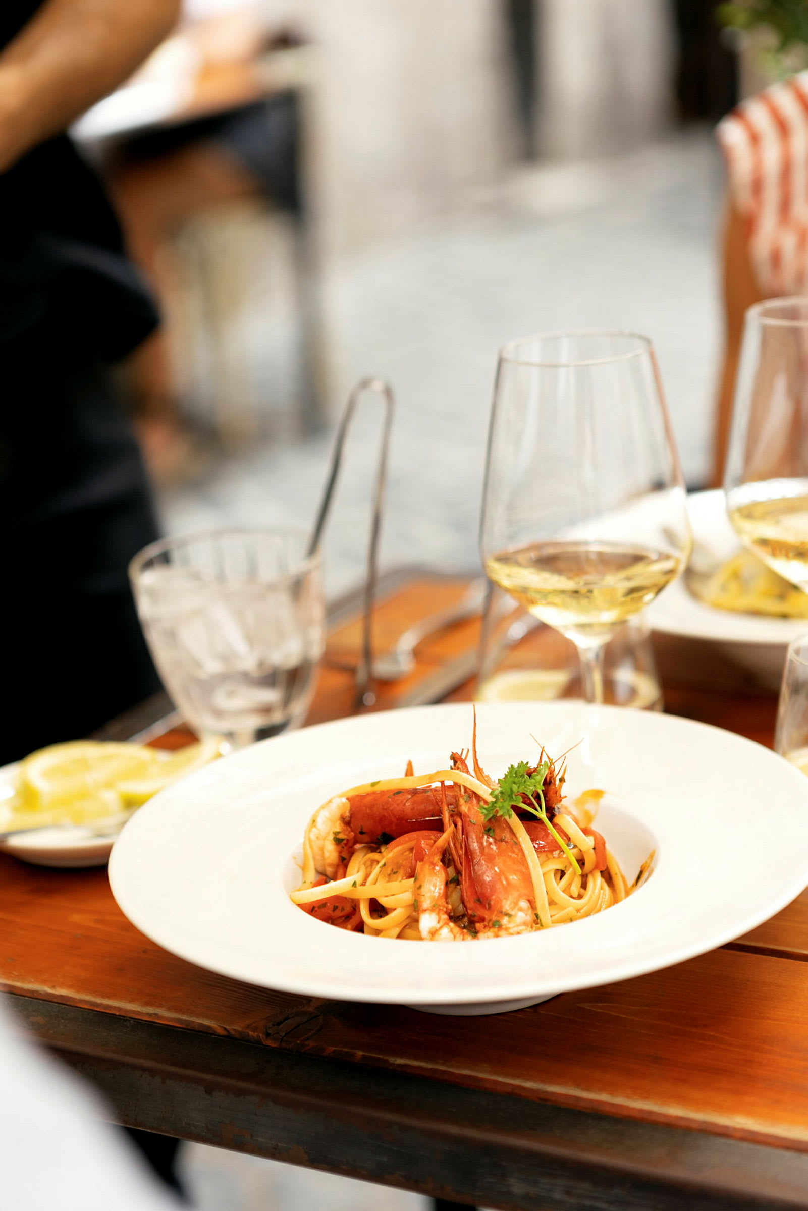 En tallerken med pasta og skaldyr på et træbord, omgivet af glas og bestik. (AI-genereret tekst)
