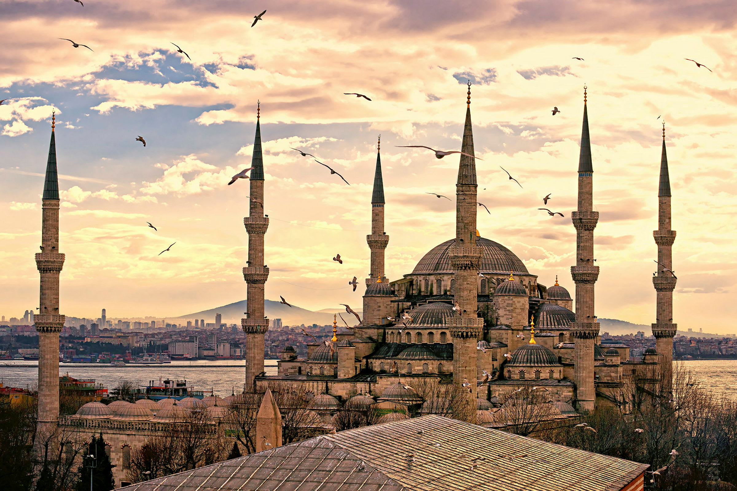 Billede af en stor moské med høje minareter og omkringliggende arkitektur mod en baggrund af himmel og by. (AI-genereret tekst)