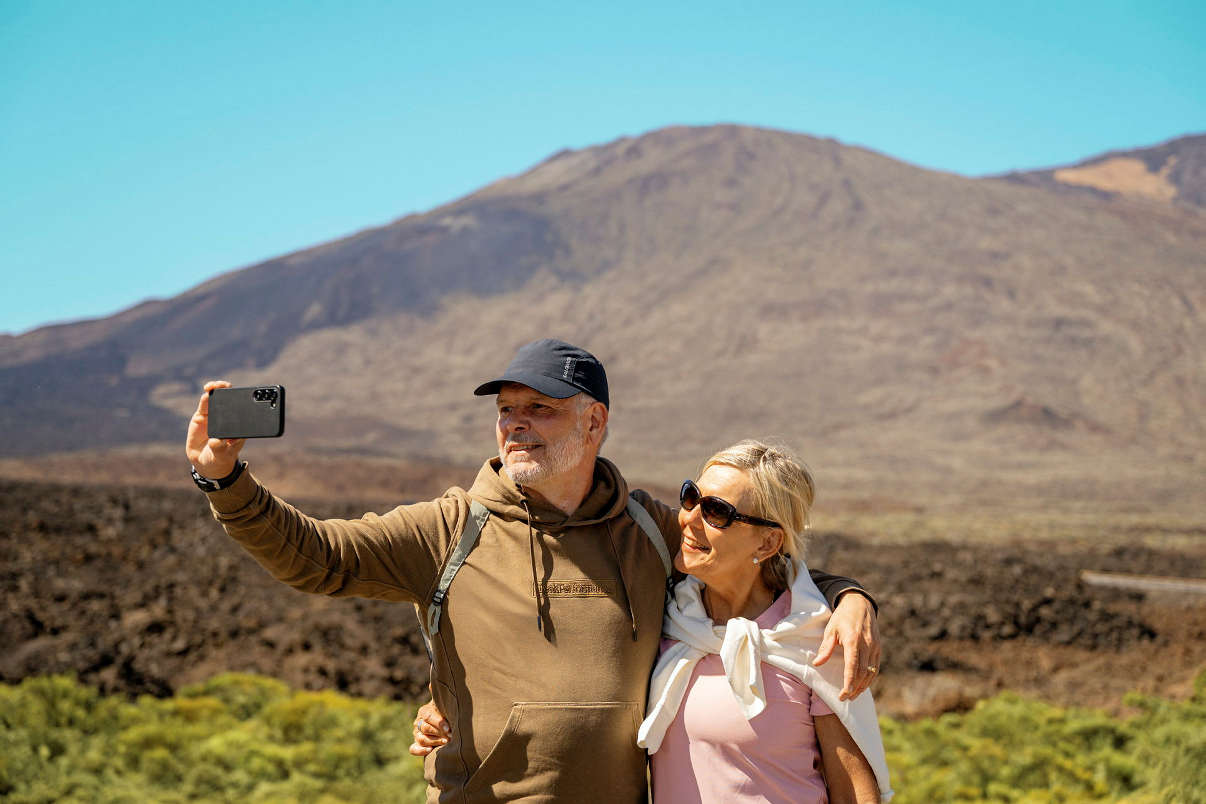 To personer tager en selfie foran et bjerg i solskinsvejr. (AI-genereret tekst)