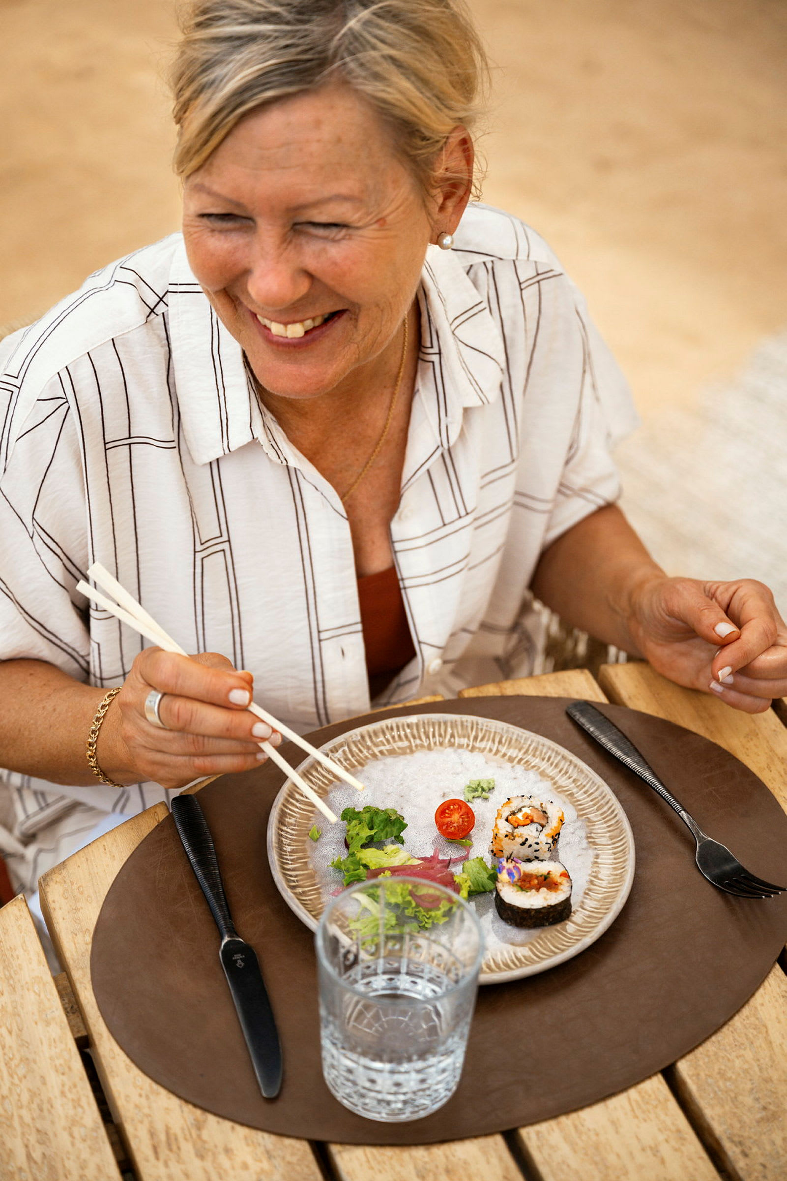En person spiser sushi ved et bord med en tallerken og et glas vand foran sig. (AI-genereret tekst)
