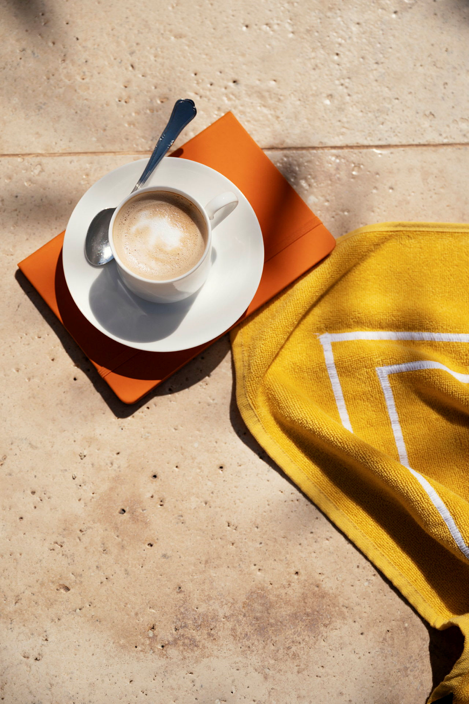 En kop kaffe med en ske ligger på en tallerken med en orange bog og et gult håndklæde. (AI-genereret tekst)