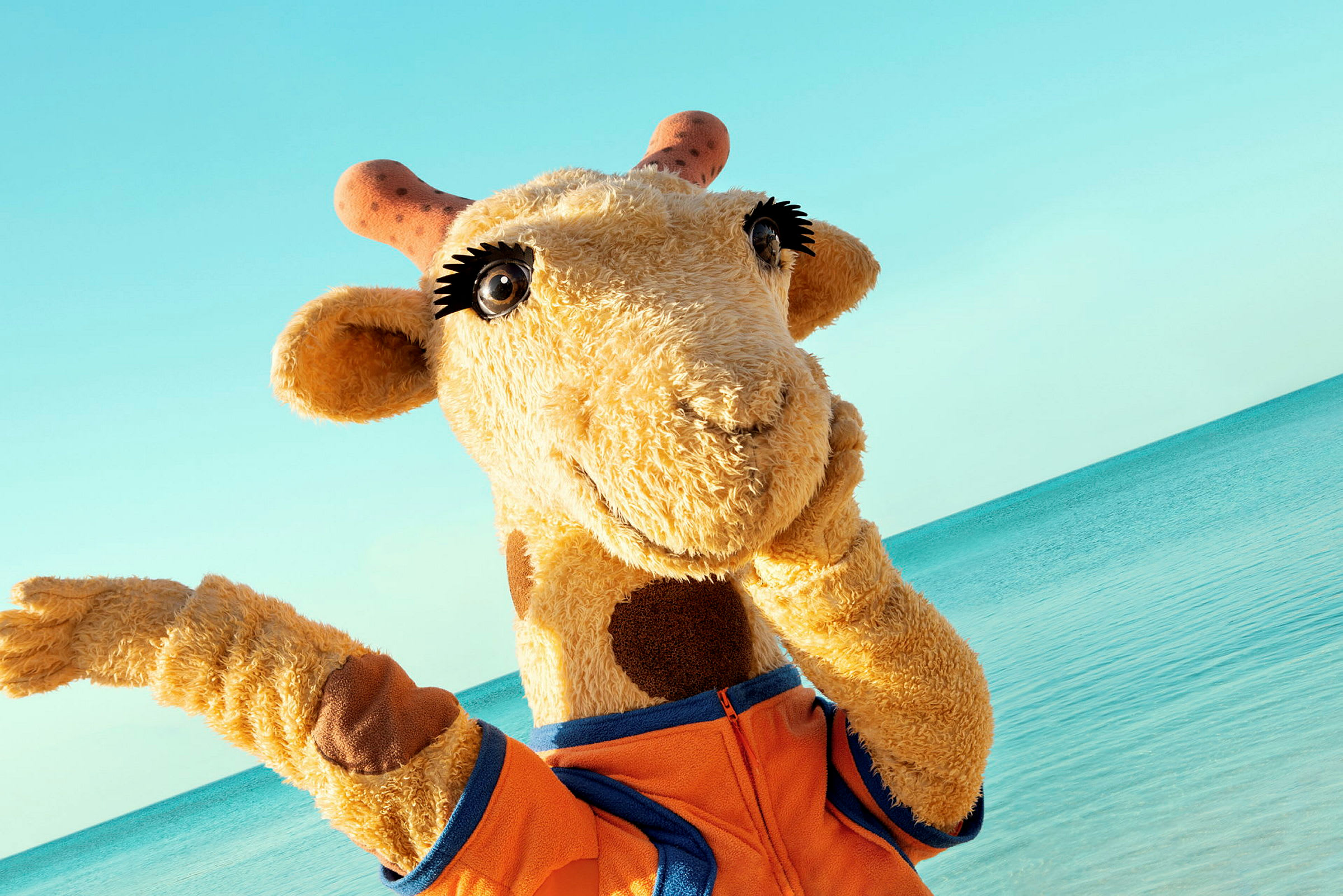 Maskotten giraf ved stranden. (AI-genereret tekst)