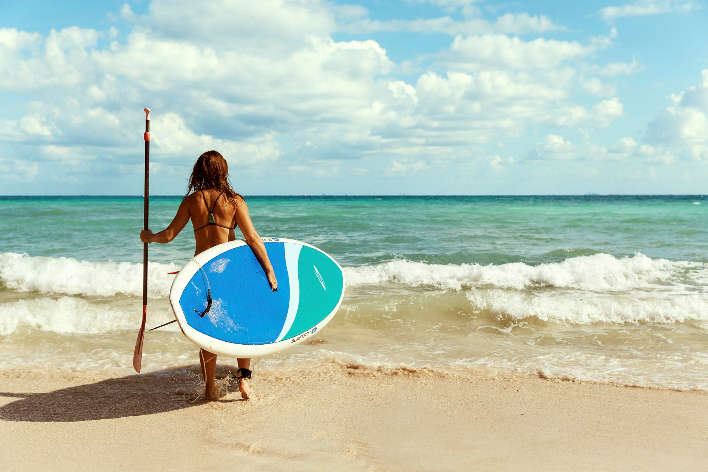 Person med våddragt og paddleboard på vej mod havet. (AI-genereret tekst)