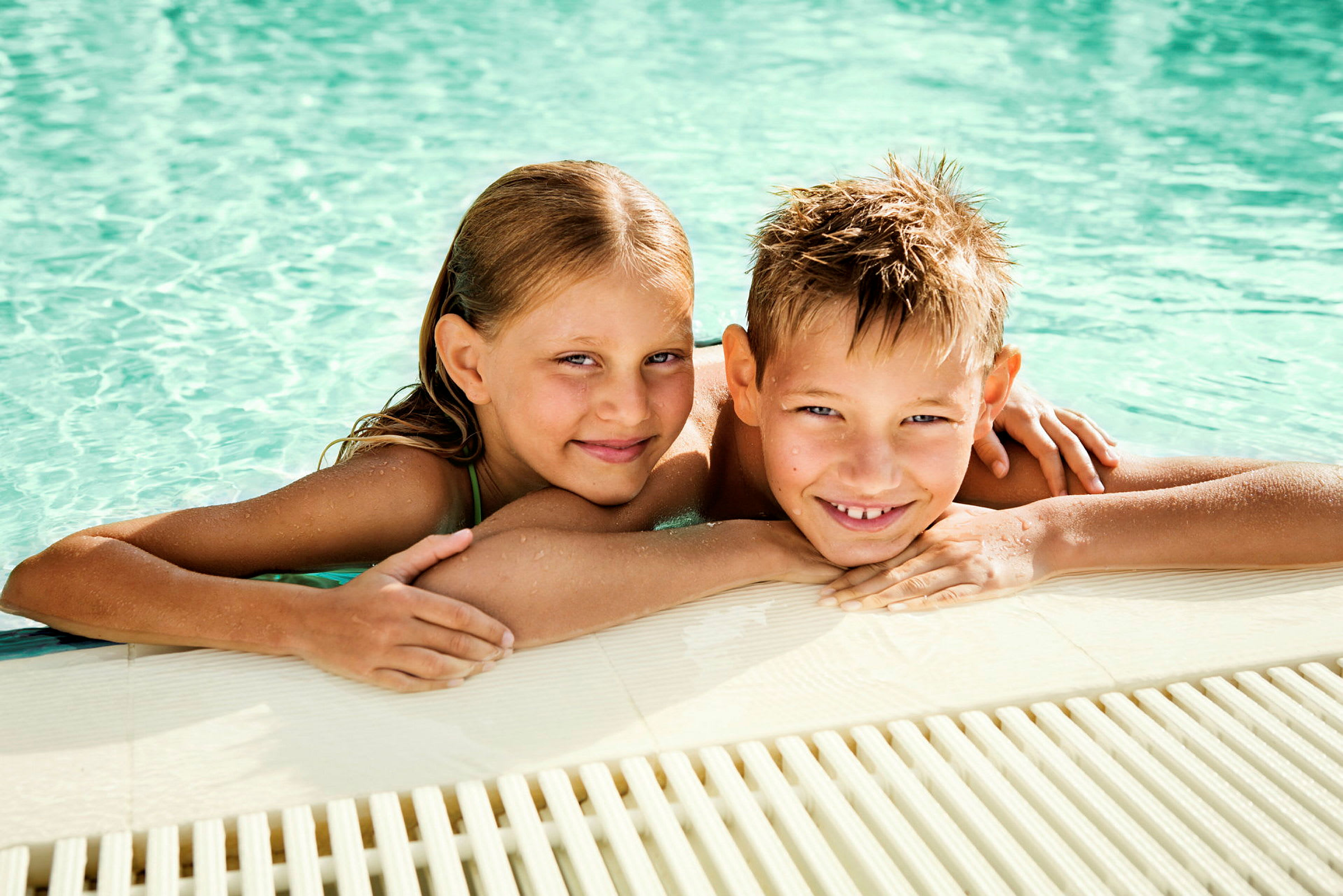 To personer ligger ved kanten af en pool med vandet i baggrunden. (AI-genereret tekst)