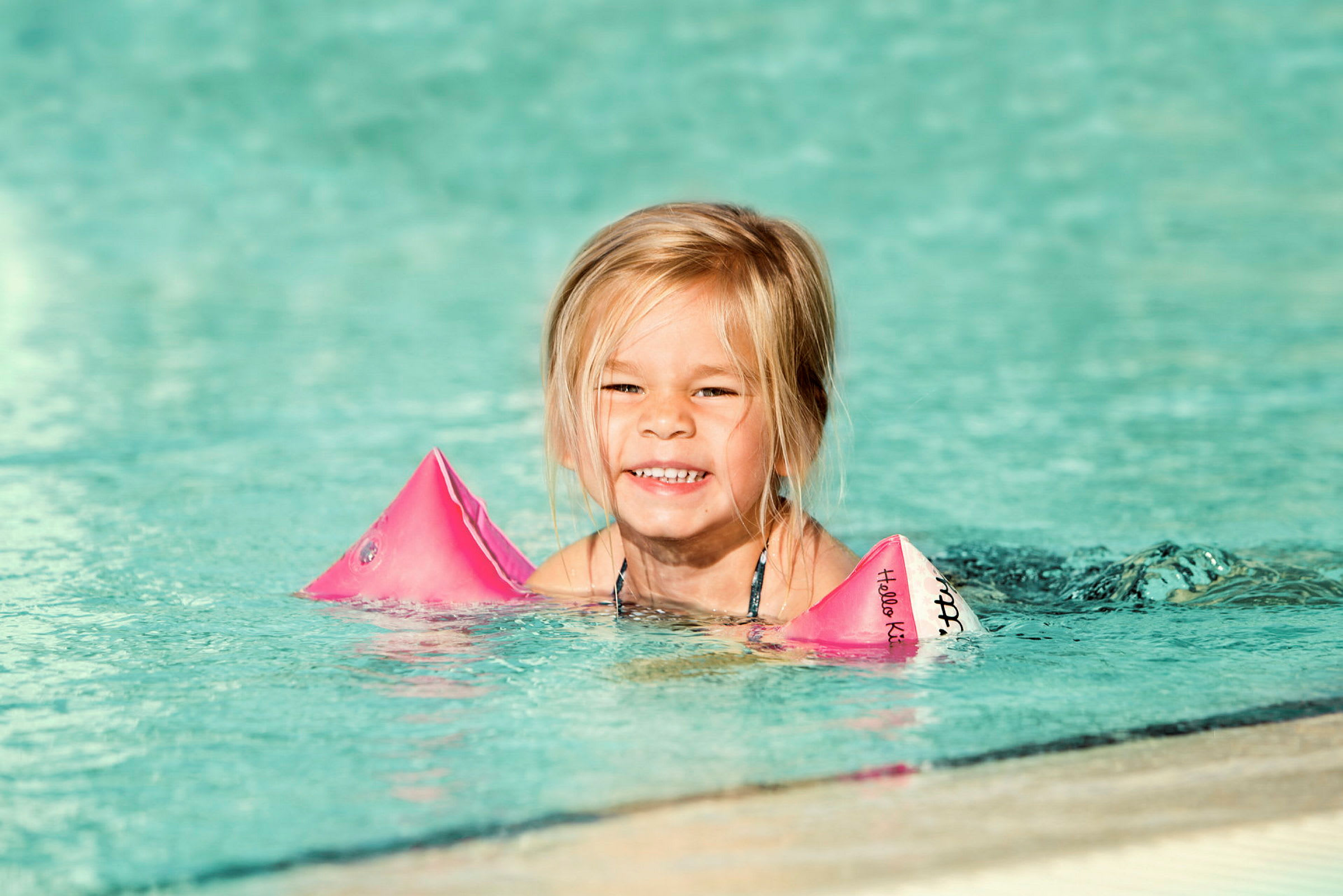 Et barn i en pool med pink armringe. (AI-genereret tekst)