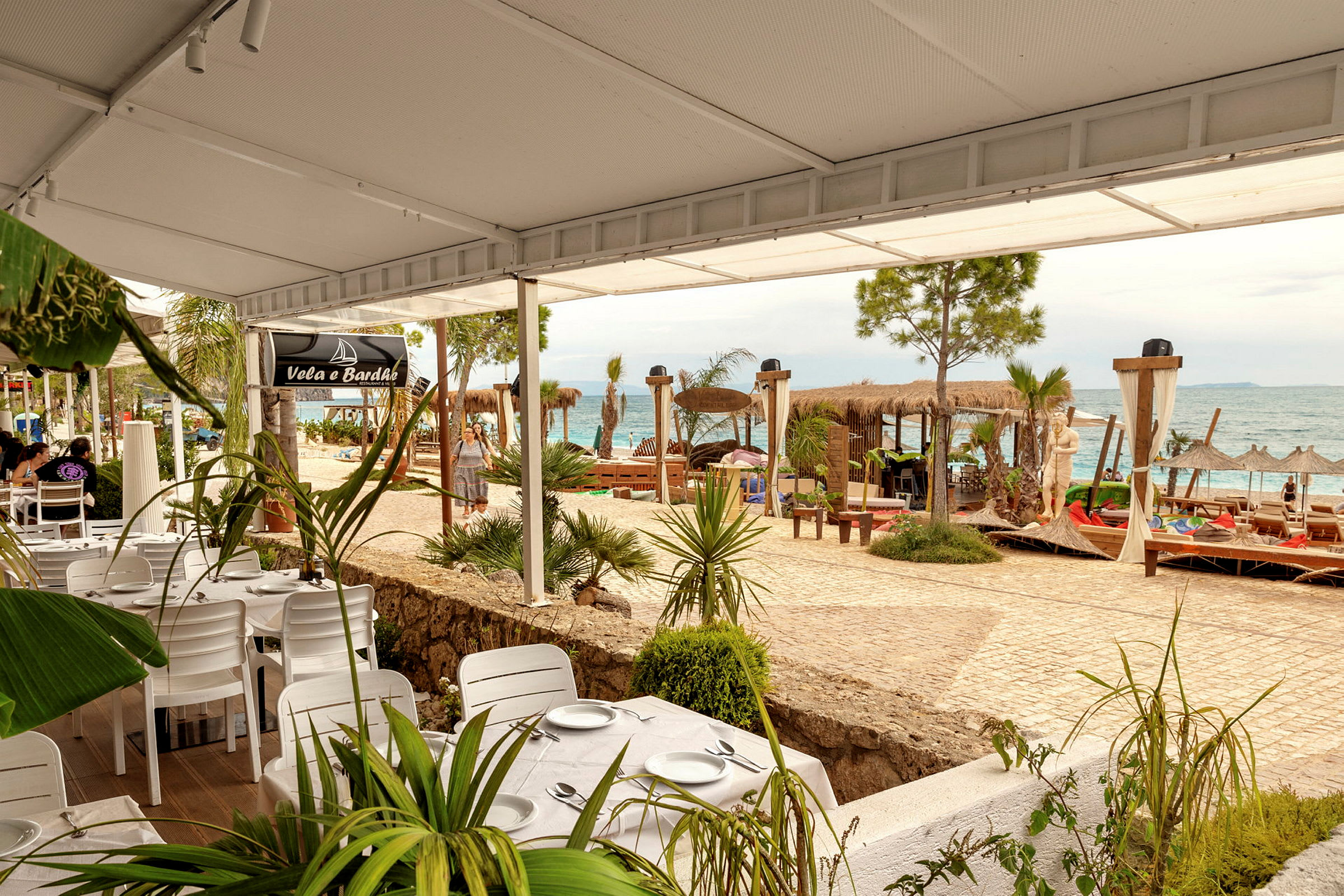 Strandnær restaurant med hvide borde og stole, havudsigt og liggestole. (AI-genereret tekst)