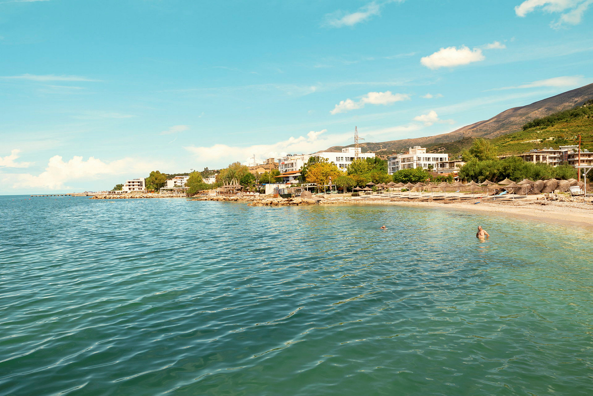 En strand med klart vand og bygninger i baggrunden. (AI-genereret tekst)