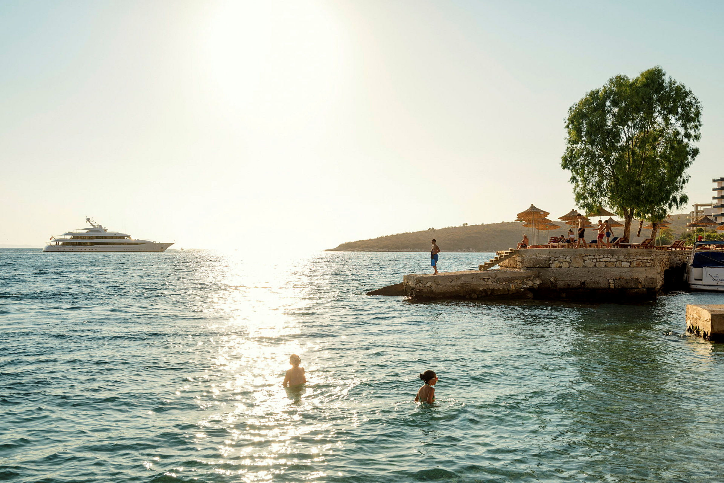 Folk svømmer i havet nær en mole med solsenge og parasoller. (AI-genereret tekst)