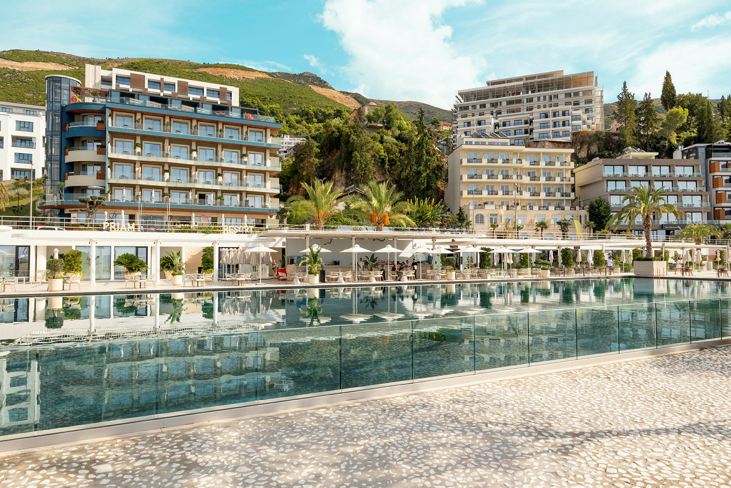Hotelkompleks med pool i fokus, omgivet af grønt og bygninger. (AI-genereret tekst)