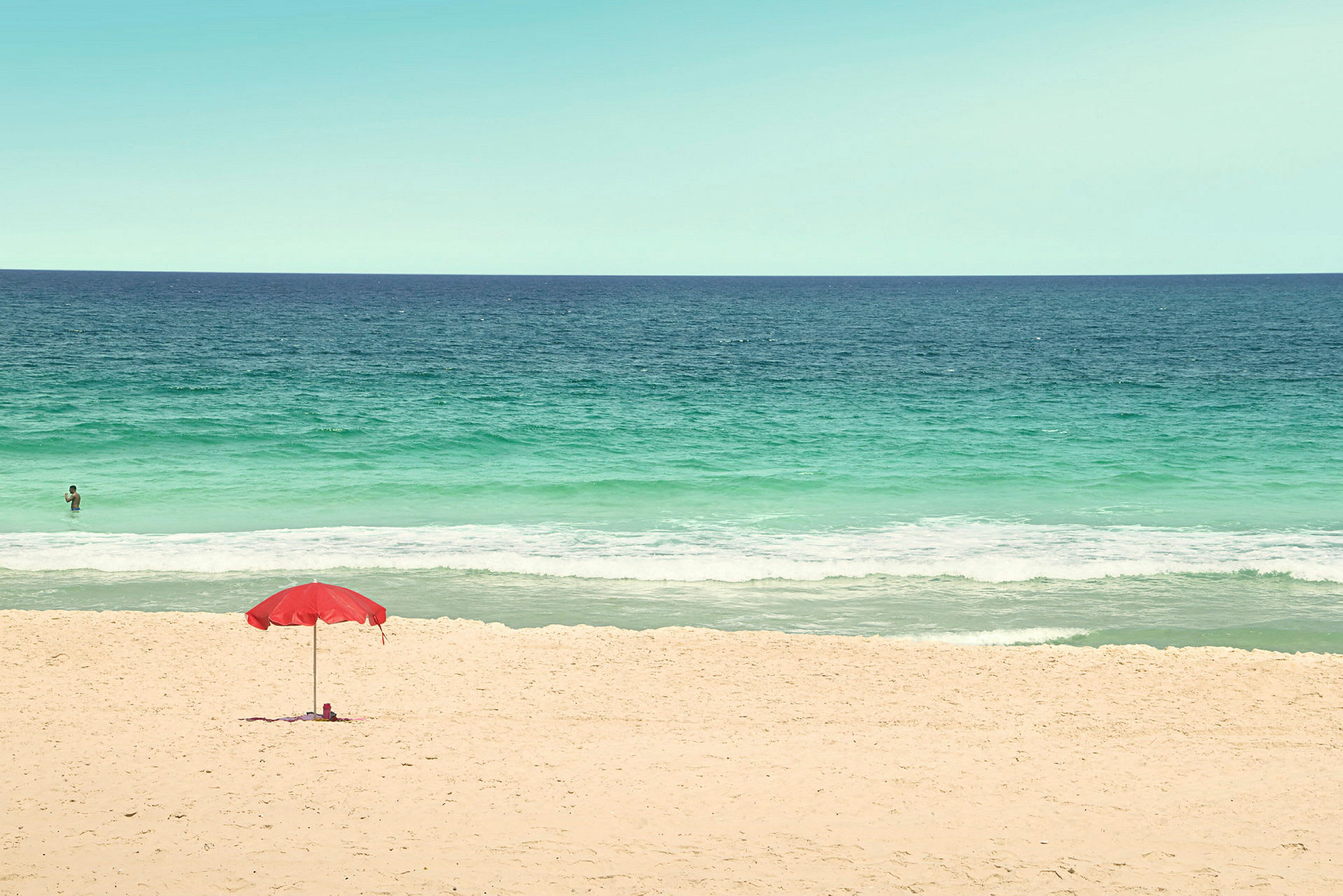 En sandstrand med en rød parasol og bølgende hav i baggrunden. (AI-genereret tekst)
