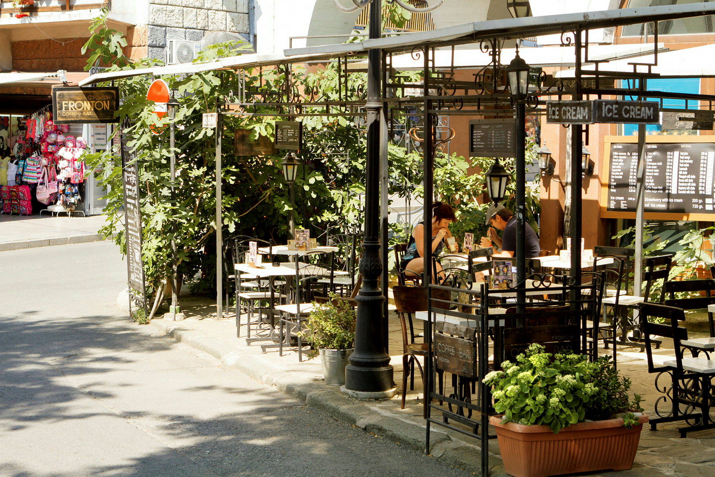 Udendørs café med planter og borde samt menutavler. (AI-genereret tekst)