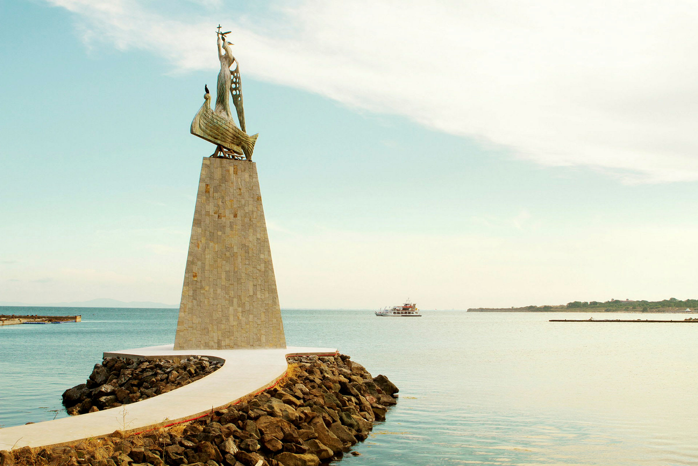 Et monument med en skulptur af et skib, beliggende ved en kaj omgivet af vand. (AI-genereret tekst)