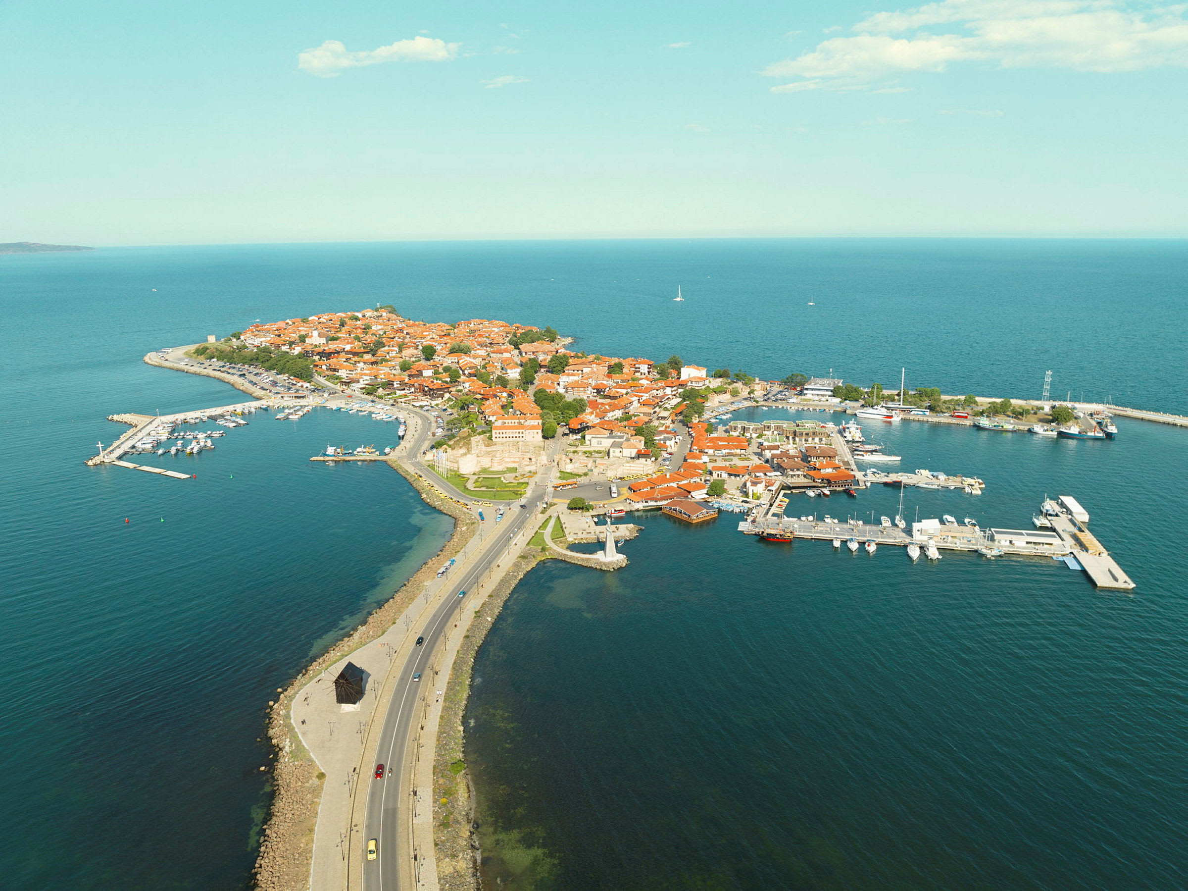 Luftfoto af en halvø med røde tage og havn. (AI-genereret tekst)