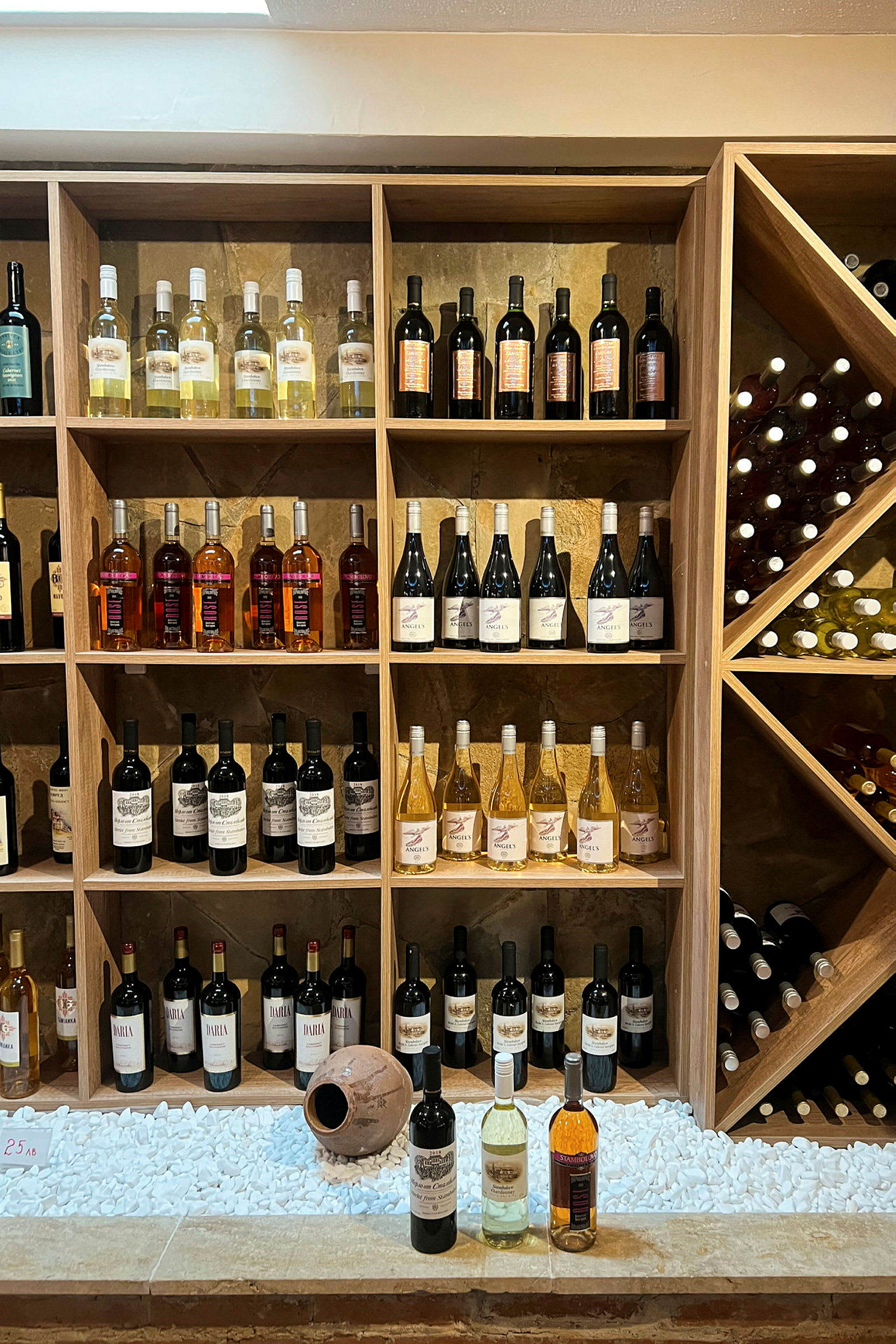 En væg med hylder fyldt med flasker med vin i forskellige farver og sorter. (AI-genereret tekst)