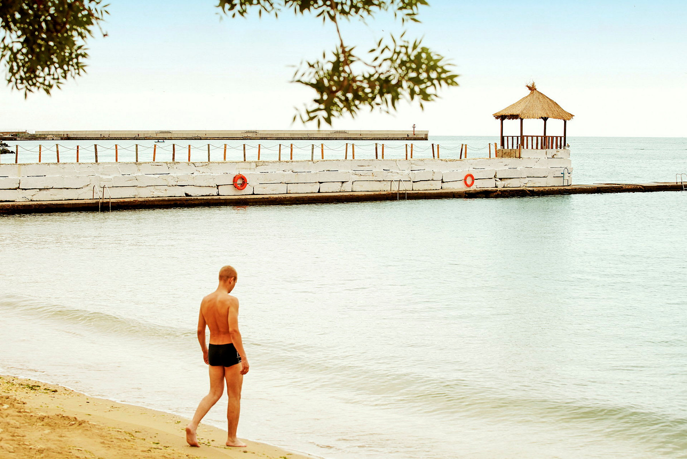 En person går på en strand ved vandet. En pavillon står på en bro. (AI-genereret tekst)