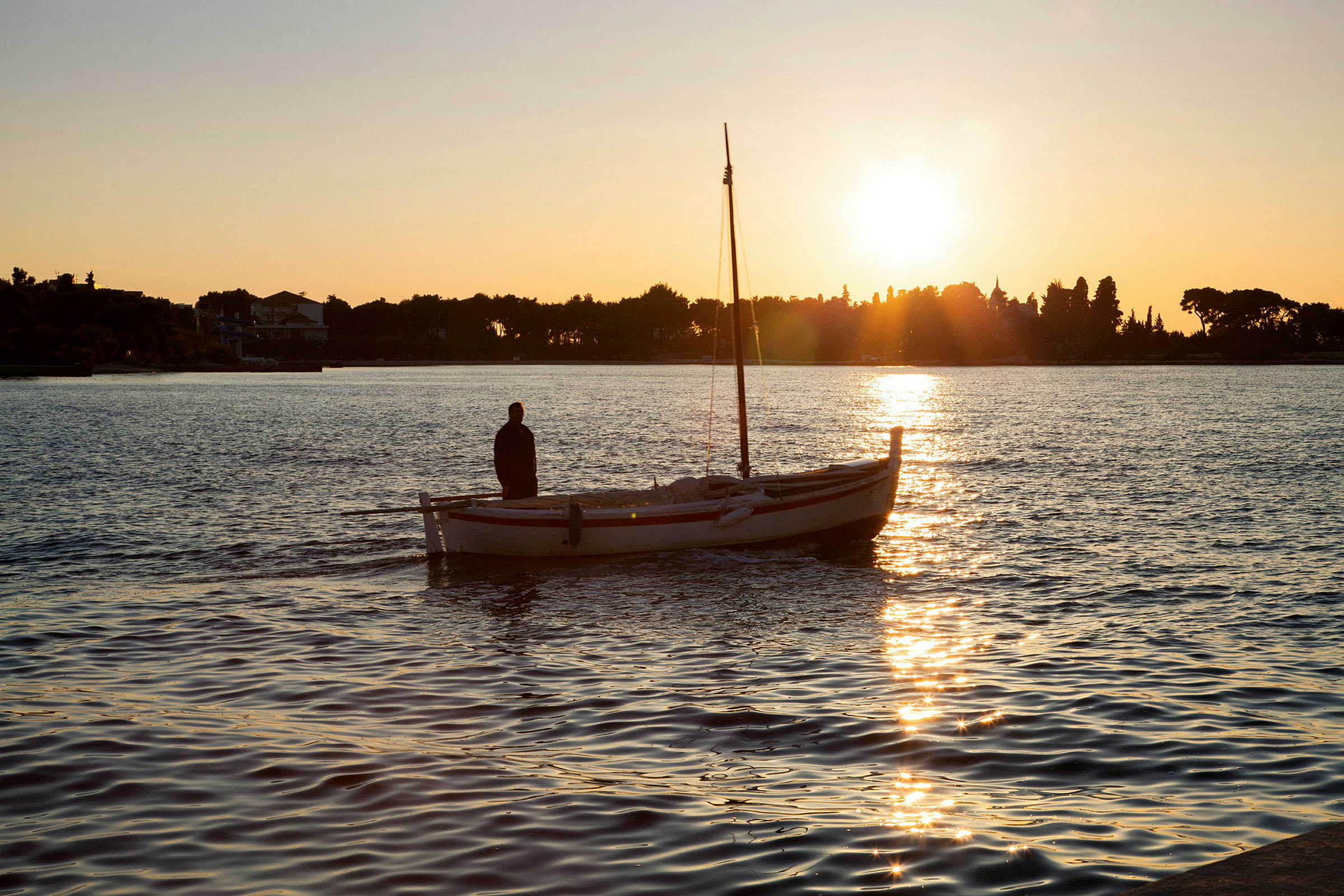 Mand står på lille båd i vandet ved solnedgang. (AI-genereret tekst)