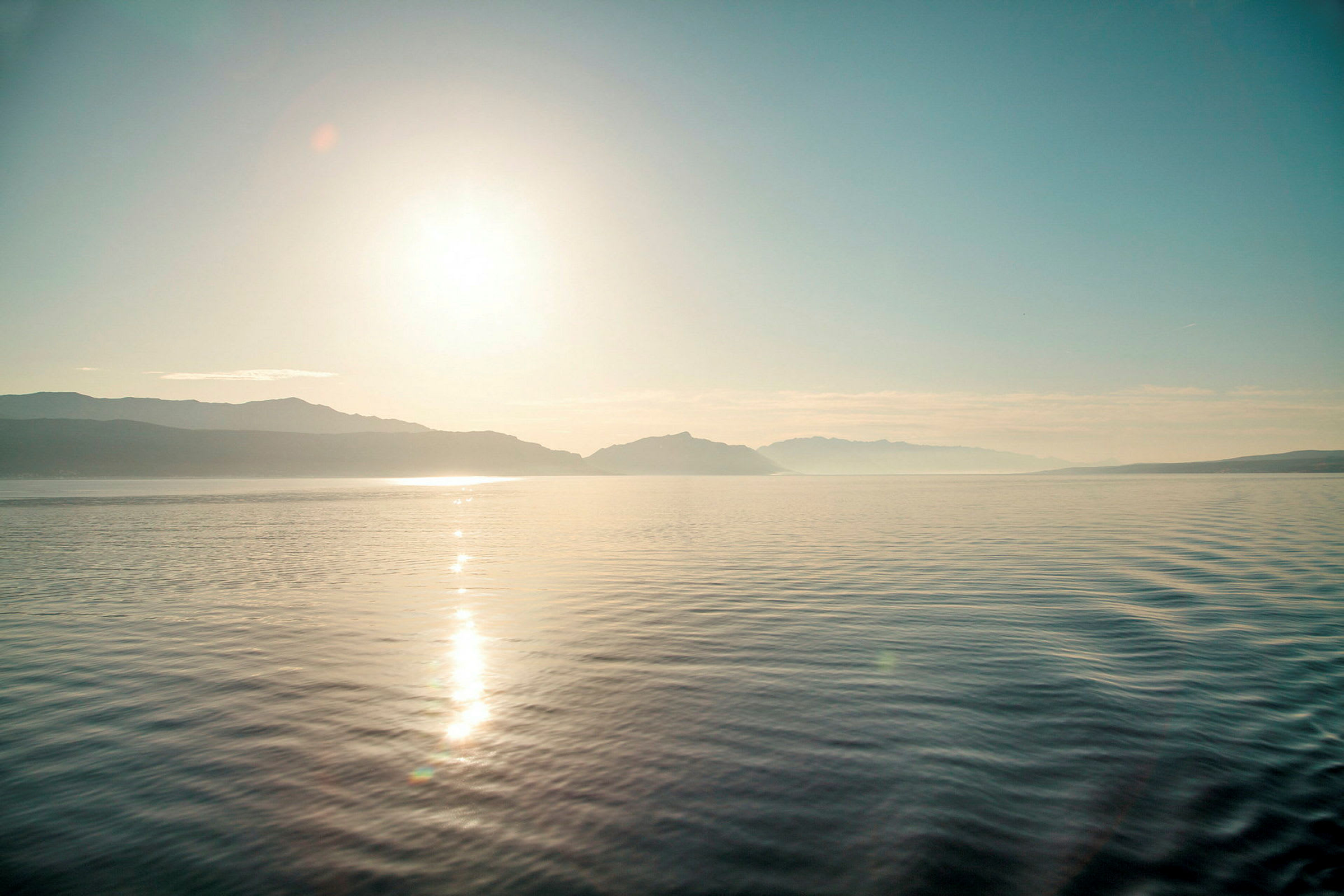 Solnedgang over en stille sø med bjerge i baggrunden. (AI-genereret tekst)