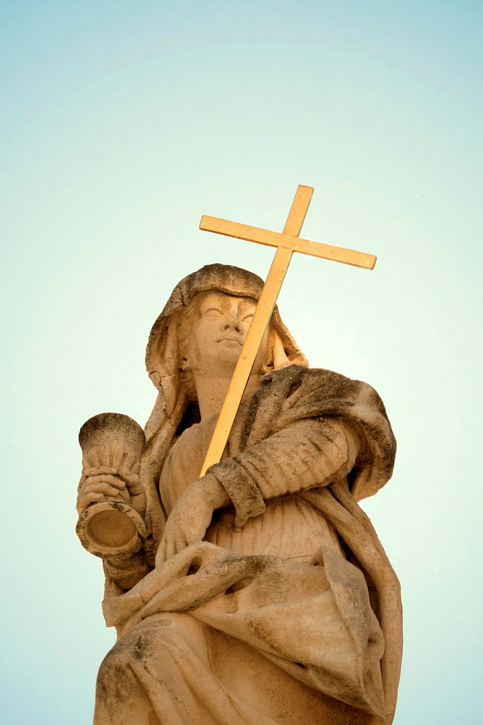 Statue af en person med et guldkors og bæger. (AI-genereret tekst)