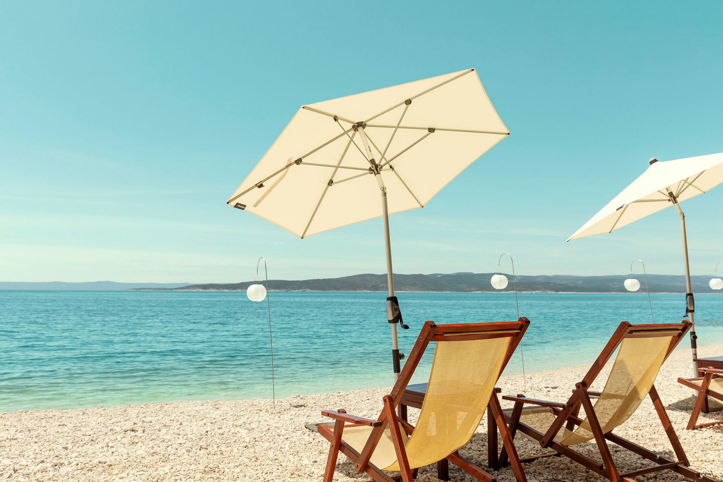 Liggestole og parasoller ved stranden med havet i baggrunden. (AI-genereret tekst)